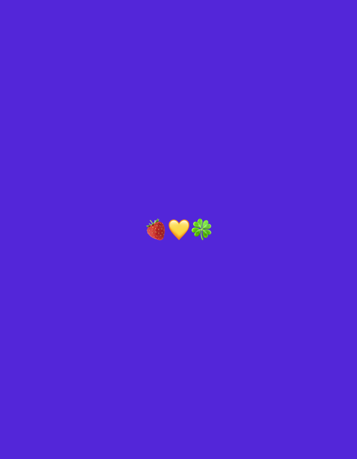 A strawberry emoji, a yellow heart emoji, and a four-leaf clover emoji are centrally located on a plain purple background. The objects are arranged horizontally.