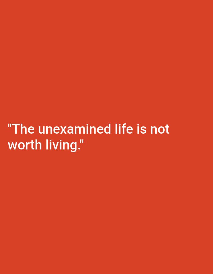 The image is a minimalist photograph with a plain, vibrant orange background. Centered on the lower half of the frame, in white, sans-serif font, is the quote: "The unexamined life is not worth living." There are no other discernible objects or people in the image. The location in Nowa Wieś Książęca, Poland is not identifiable from the visual information provided.