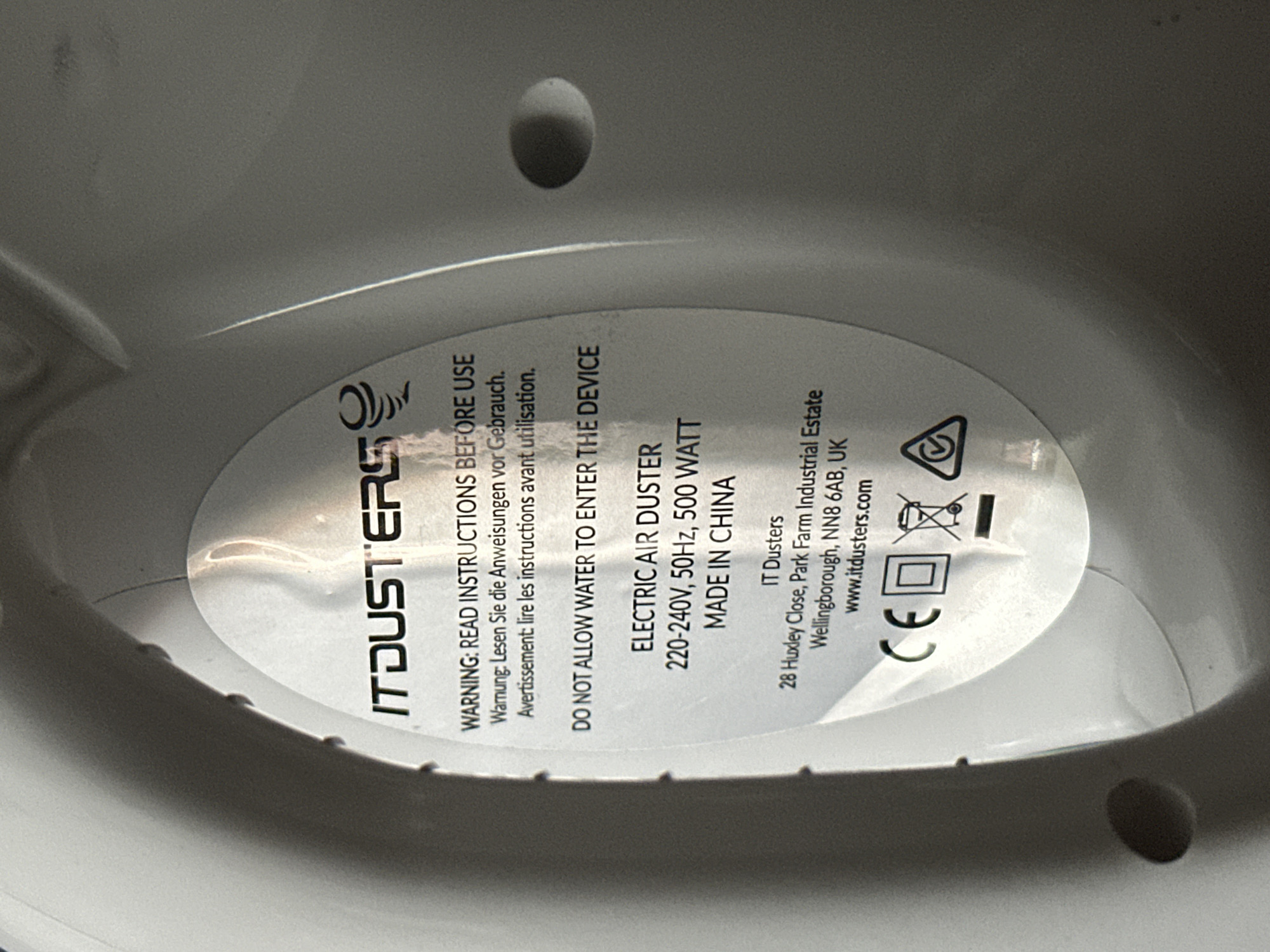 The image shows a close-up of the underside of an IT Dusters device. The label displays warnings to read instructions before use and not allow water to enter the device. It identifies the device as an electric air duster, with specifications of 220-240V, 50Hz, and 500 Watt, and indicates that it was made in China. The label also provides the address of IT Dusters: 28 Huxley Close, Park Farm Industrial Estate, Wellingborough, NN8 6AB, UK and their website. The image also shows recycling, CE, and double insulation symbols. The location of Sarcelles, France is not found within this image.