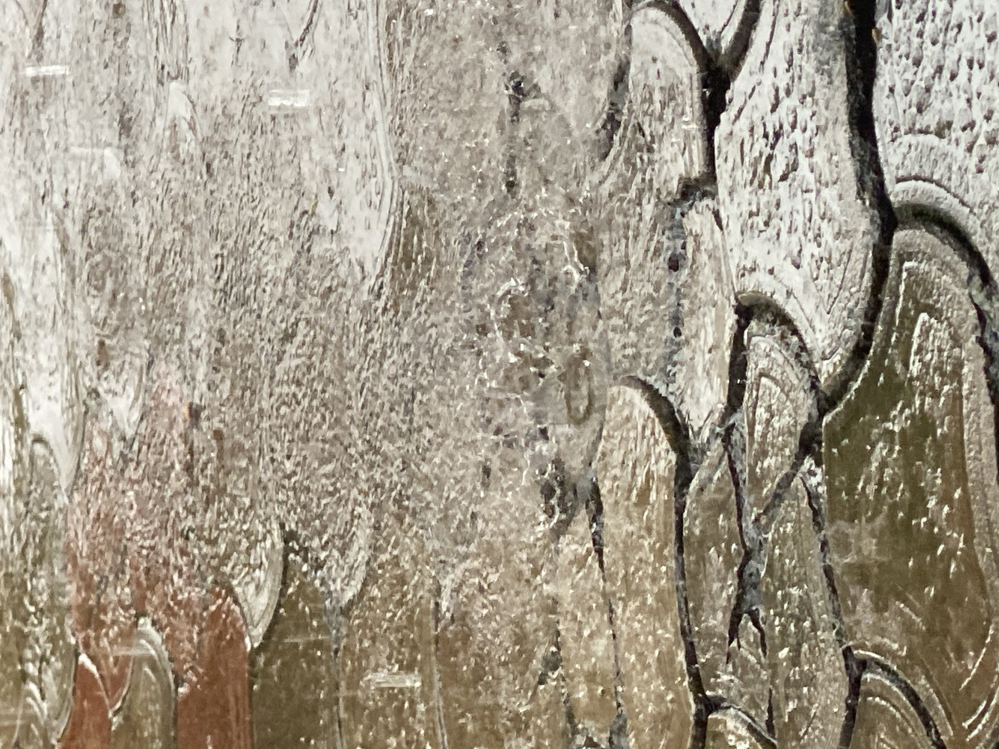 The image is a close-up shot of textured glass, possibly a window or decorative panel. The glass has a patterned surface with raised, curved elements separated by darker lines, creating a somewhat abstract design. The left side of the glass has a different texture, appearing more granular or frosted. The overall color palette is muted, with shades of beige, gray, and hints of brown. The image does not provide any information about the city of Maigizo, Nigeria, nor does it depict any people, subjects, objects, actions, or interactions related to that location.