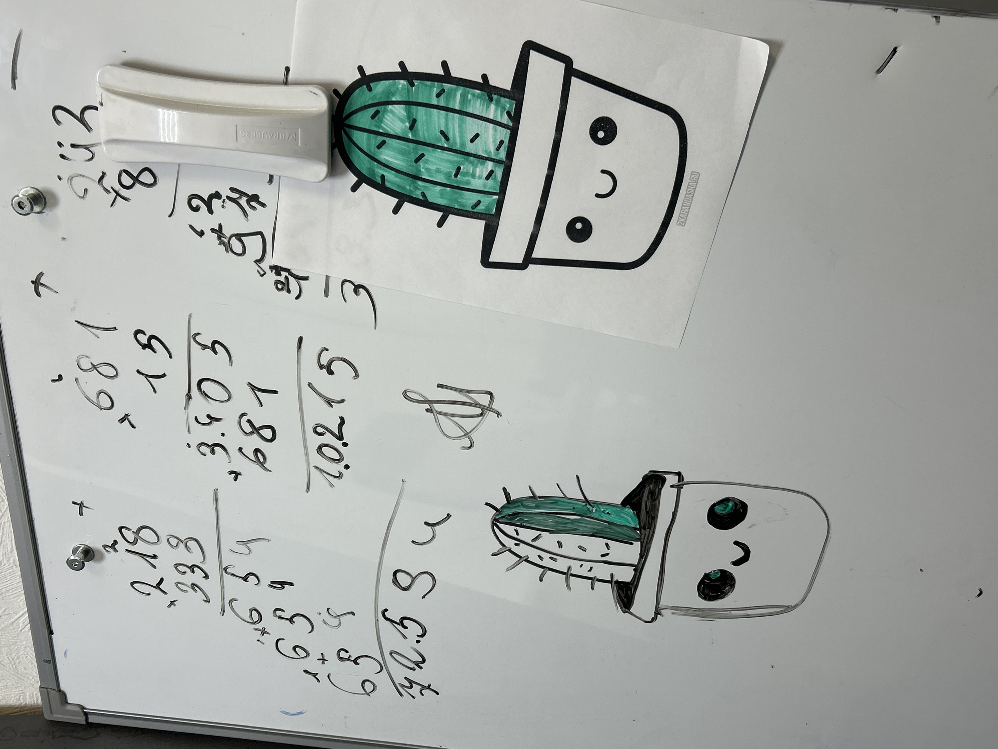 The image displays a close-up of a whiteboard, suggesting an educational or creative setting in Chaikovsky, Russia. The board is actively in use, covered with various handwritten mathematical calculations and adorned with cheerful cactus drawings.
In the upper left quadrant, a white rectangular whiteboard eraser, branded "BRAUBERG," is magnetically attached to the board. Below it, several handwritten numbers and arithmetic operations are visible, including addition problems. These include "+ 218 / 333" resulting in "651" (or "659" below it), and other numbers such as "72.59," "8," and "243." Another set of calculations features "+ 681 / 13," "3.405," "681," and "1.0.215," followed by a distinctive, looped signature or doodle.
Two cartoon cactus drawings add a playful element to the board. In the upper right, a printed image shows a green cactus with black spikes in a white pot, featuring black circular eyes and a smiling mouth. The small text "2KARANDASHA.RU" is visible in the bottom corner of this print. Below it, a similar hand-drawn cactus in a pot is sketched directly onto the whiteboard, also with green coloring, black spikes, and a smiling face. Two silver, circular magnets are also visible, holding down what appears to be paper or simply adhering to the board. The overall scene suggests a blend of learning and personal expression.