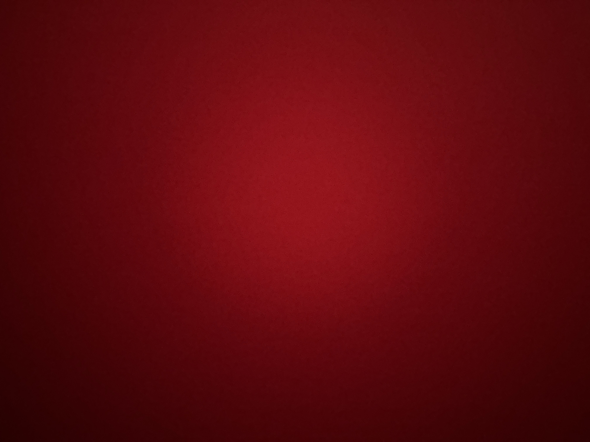 This media file is a photograph of a textured, dark red background with a subtle gradient. The lighting is dim, creating a vignetting effect where the edges are darker than the center. There are no discernible subjects, objects, or activities taking place. The texture of the background appears to be fine-grained, perhaps resembling fabric or a matte paper. The color is a deep, rich red. The overall impression is one of simplicity and focus on the color and texture of the background. There is no visible text.