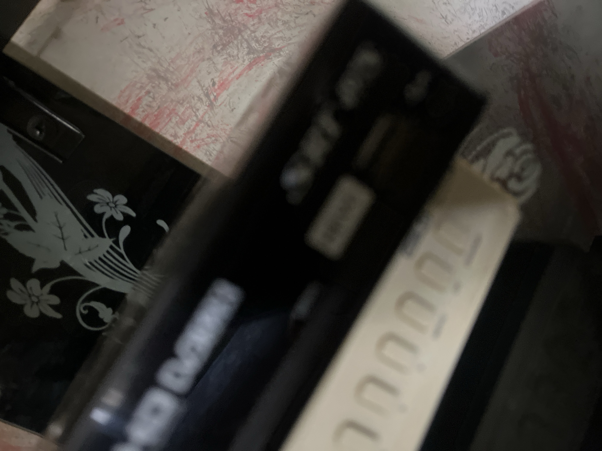 The image is a close-up, slightly blurry shot of an electronic device, possibly a DVD player or set-top box, with text that is partially visible. The device is black with some silver accents and what appears to be a decorative element on the top, which seems to be a stylized bird and flowers etched or printed on a dark background. Below the device, there's a white surface with textured markings that look like braille or a tactile pattern. The scene is lit from above and the background is dark, suggesting an indoor setting. There is no information in the image to indicate the location in the city of Jalingo, Nigeria.