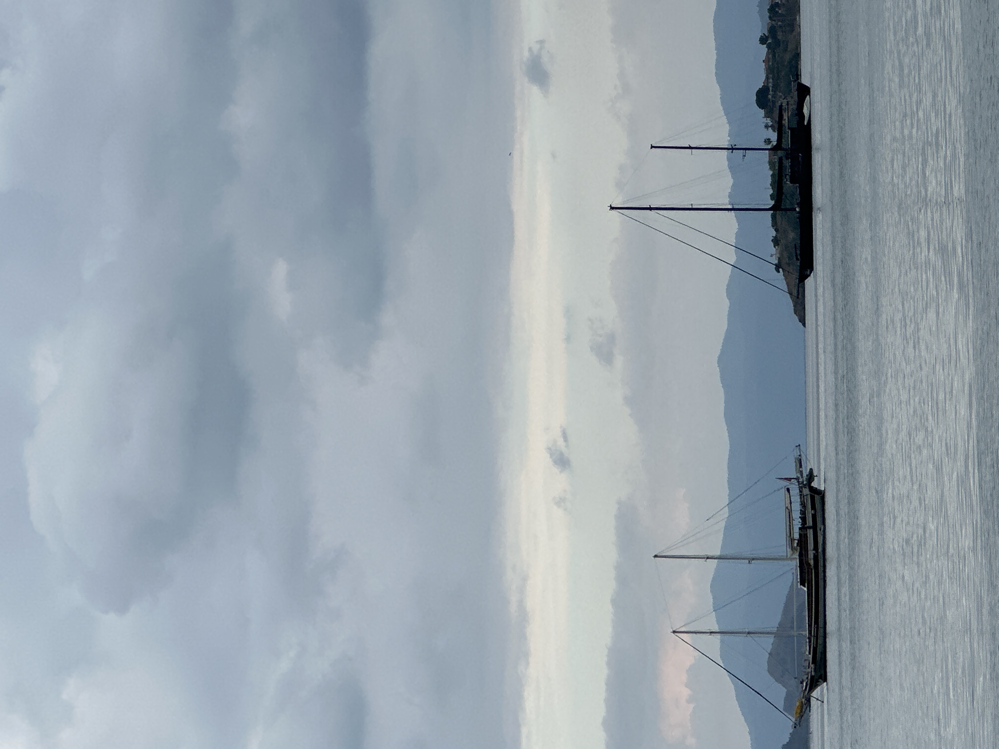The image shows a cloudy sky over water with two sailboats docked near the shore, likely in Fethiye, Turkey. Mountains are visible in the background.