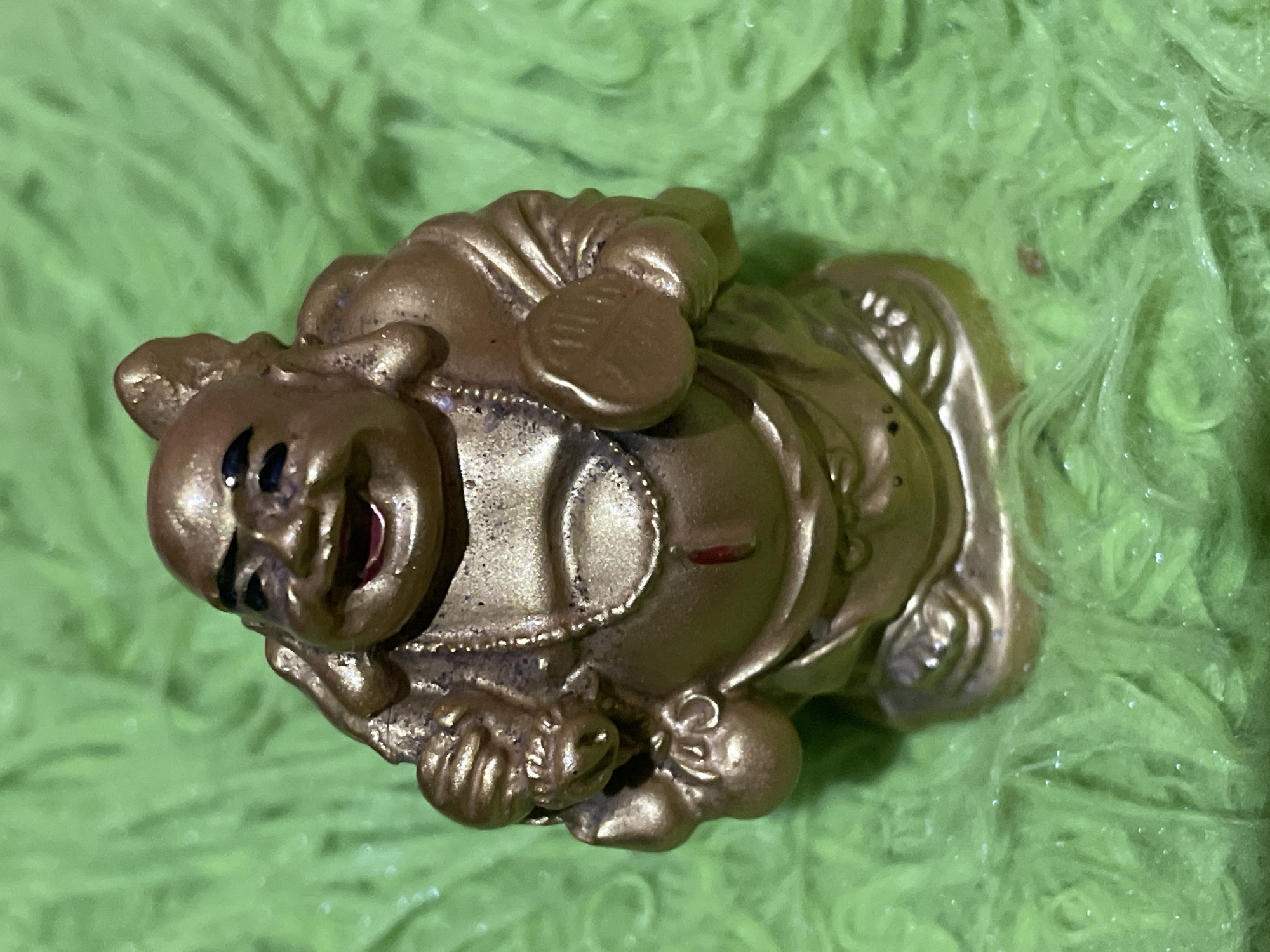A golden statue of a laughing Buddha is resting on a lime green, fuzzy surface. The statue is oriented horizontally, with the Buddha's face toward the top left of the frame. The environment is undetermined; the location of Davao City, Philippines is not visually discernible.