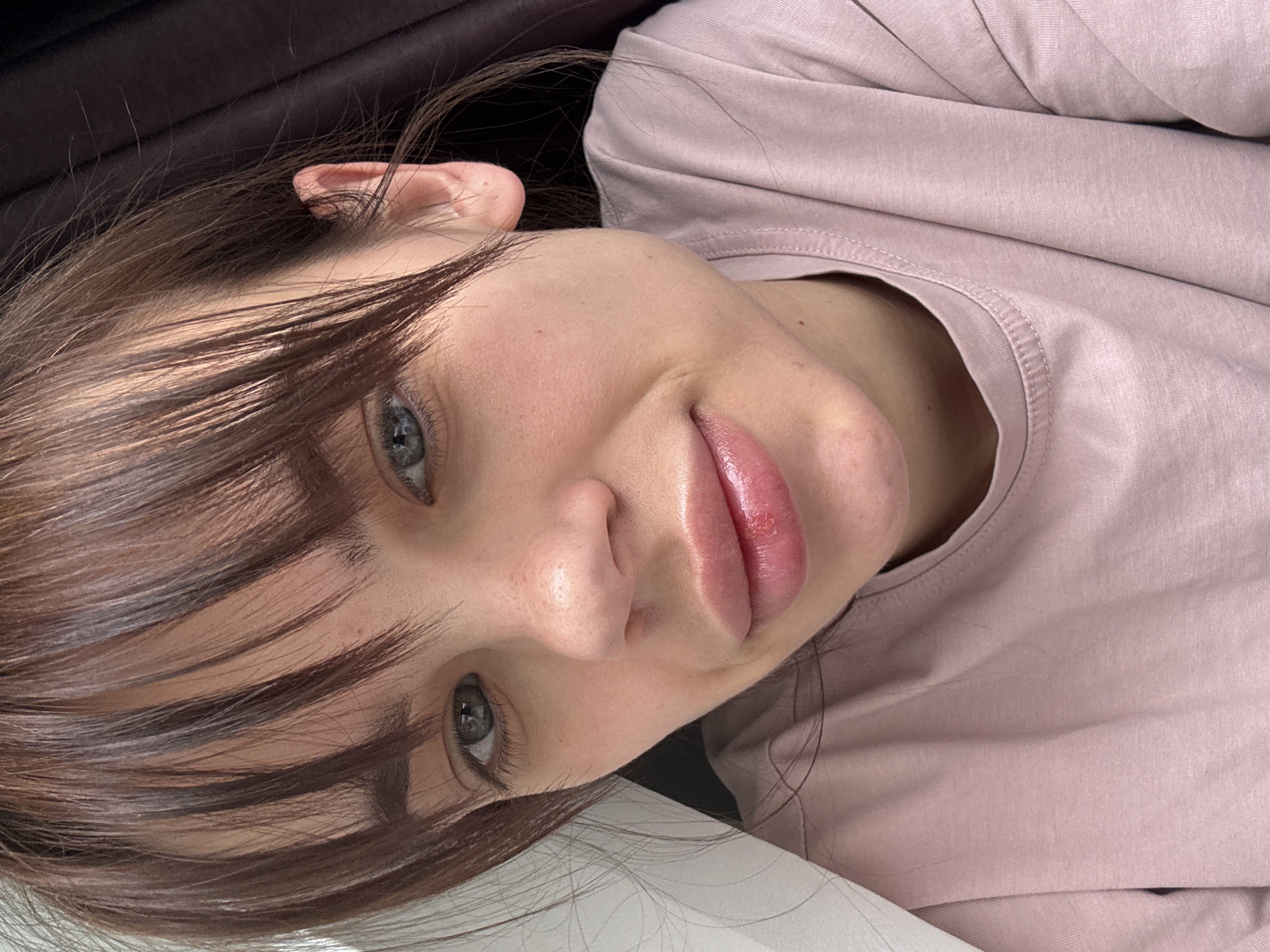 A close-up, angled portrait of a woman with light skin, gray-blue eyes, and dark brown hair with bangs. She wears a pale pink long-sleeved shirt. The background appears to be a dark, possibly black, surface. There is also a section of white surface visible at the bottom. There is no information available to indicate a location within Rostov-on-Don, Russia.