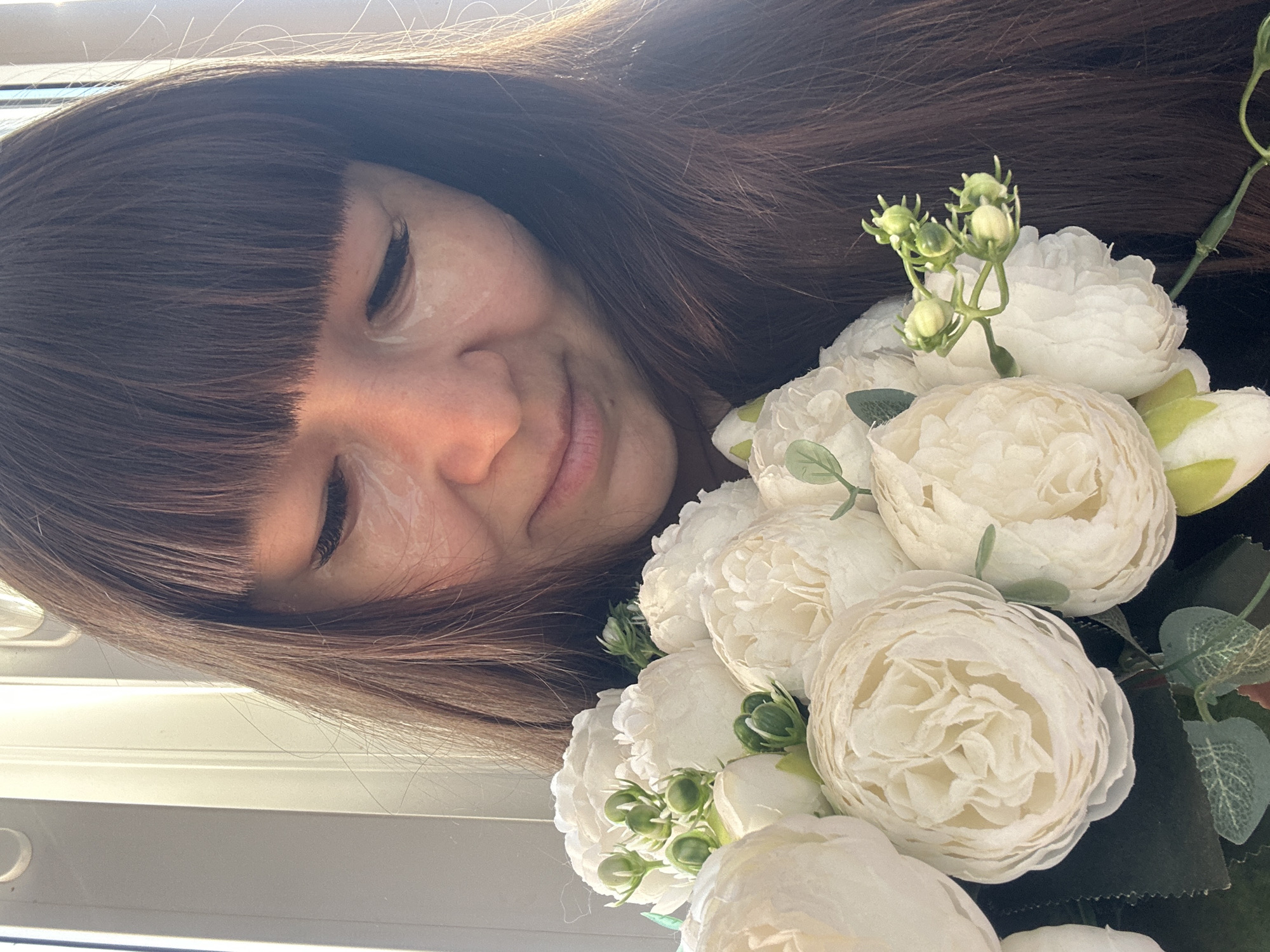 A woman with brown hair and bangs is holding a bouquet of white flowers. The background appears to be a window. The location is claimed to be Chaikovsky, Russia, but there are no elements within the image to confirm this.