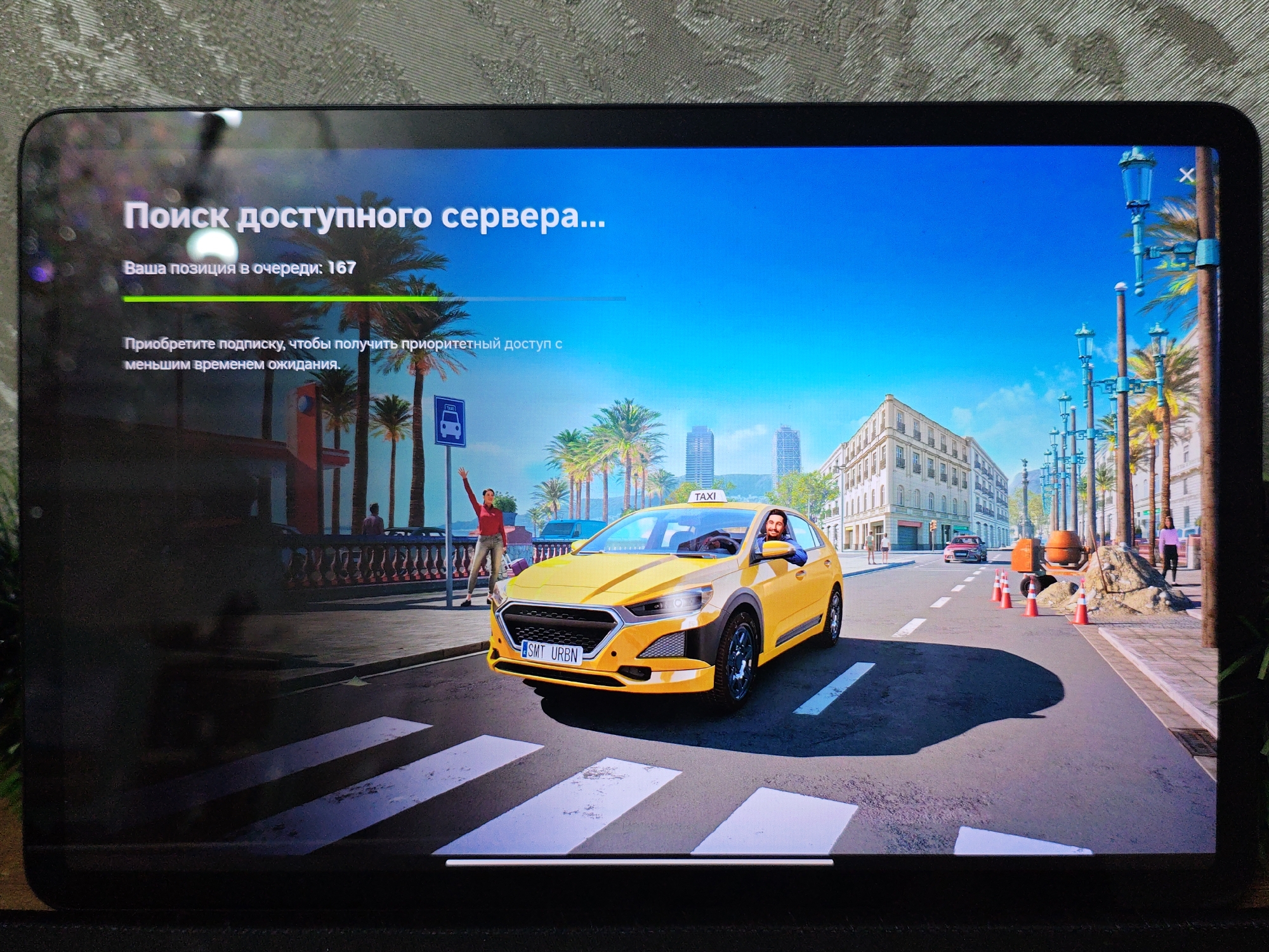 A tablet displays a video game loading screen with a vibrant cityscape. The text in Russian reads "Searching for an available server..." and "Your position in the queue: 167". Below this, it states "Subscribe to get priority access with less waiting time." The scene depicts a yellow taxi with a driver smiling at the viewer, stopped at a crosswalk. A woman in red is waving from the sidewalk, and palm trees line the street. In the background, there are buildings and construction equipment. The game appears to be set in a sunny, Mediterranean-style city. There is no indication of Baku City, Azerbaijan in the image.