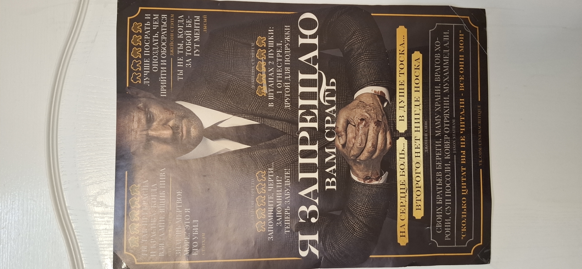 The image is a close-up shot of a poster featuring a man in a dark suit. The text on the poster is in Russian. The poster also contains various quotes attributed to Jason Statham and other figures. There is no discernible location like the city of Chaikovsky, Russia.
