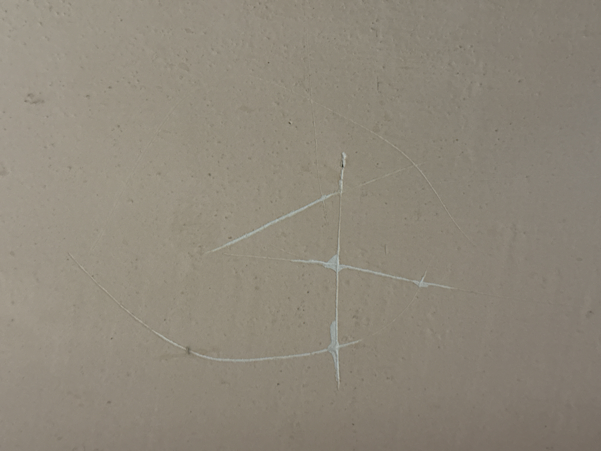 This media file is a close-up, overhead shot of a textured, light-colored wall, possibly plaster or concrete. The surface is speckled with small dark dots and has some subtle variations in tone, suggesting it is a matte finish.
The primary subject is a drawing scratched into the wall with white paint. The drawing is abstract and geometric, resembling a stylized number four or a compass rose. It features a vertical line intersected by a horizontal line, with diagonal lines extending from the intersection point. A faint, curved line, also appearing to be part of the scratched-in drawing, arcs around the central geometric element. There are also a few lighter, faint scratches that appear to be unrelated to the painted drawing.
The lighting appears even and diffused, with no strong shadows, suggesting it might be artificial light or an overcast day. There are no discernible details about the time of day, weather, or specific location within Khimki, Russia, other than the surface itself. No people or distinct objects are visible in the frame. The overall impression is one of a simple, textured surface with a superimposed, possibly accidental or deliberate, artistic marking.