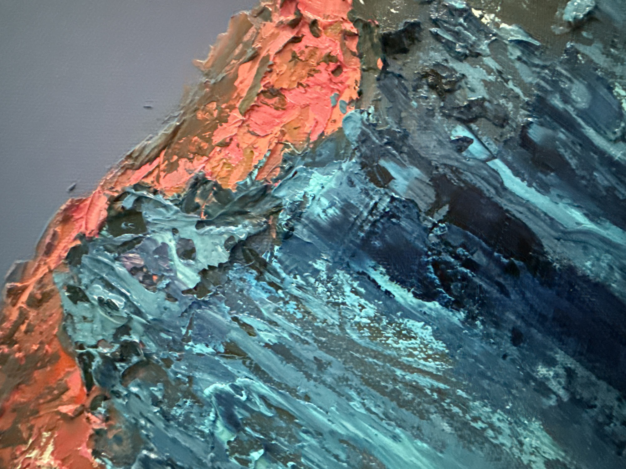 The image is a close-up, abstract painting of a mountain landscape, rendered with thick impasto strokes. The dominant colors are vibrant blues and teals, creating a textured, rocky terrain. Streaks of coral and salmon pink highlight the upper portions of the mountains, suggesting sunlight or a dramatic sky. The background is a muted, pale gray, providing a stark contrast to the energetic foreground. The painting style is highly textural, with visible brushwork and layers of paint creating a sense of depth and ruggedness. The image does not contain any specific identifiable landmarks or details that would associate it with the city of Sochi, Russia, or any other particular location. It is a stylistic representation of mountainous terrain.
