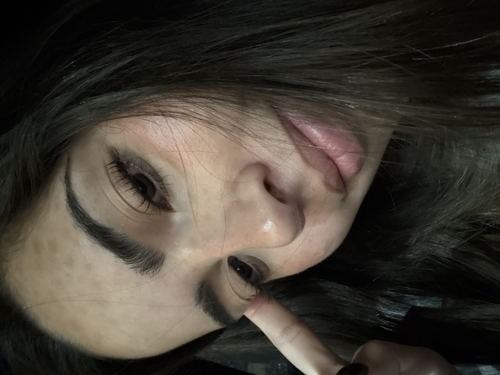 A close-up, angled selfie shows a person with dark hair, light skin, and dark eyes. The person is partially visible from the forehead to the chin. The person's finger pulls down their lower eyelid. The background is dark and undefined. The location is not discernible from the image. There is no indication that the image was taken in San Bernardino Tlaxcalancingo, Mexico.