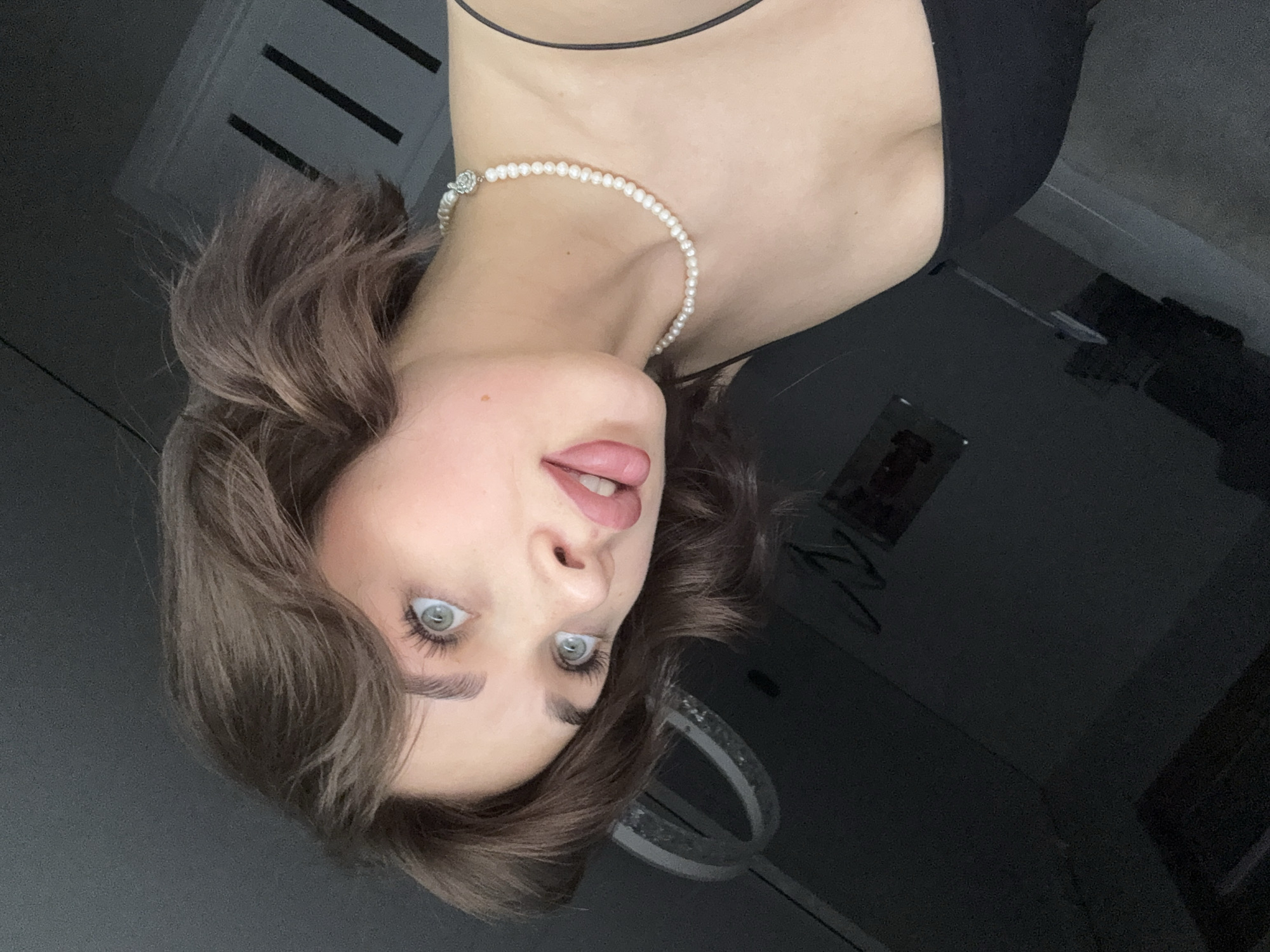 A woman with light eyes and brown hair is wearing a pearl necklace and a black top. The photo was taken indoors. The location is in the city of Лобаново, Russia.