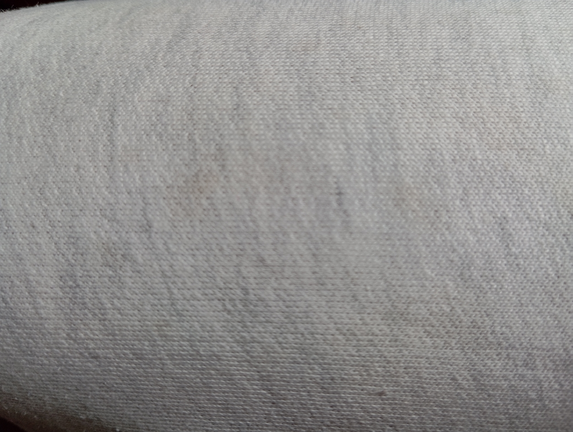 The image is a close-up, abstract shot of a textured, light-colored fabric, likely cotton or a blend. The fabric appears to be a light grey or off-white, with subtle variations in shading and a visible woven pattern of interlocking threads. There are a few faint, darker smudges or stains scattered across the surface, particularly in the central and upper-left portions of the image. The lighting is soft and diffuse, highlighting the texture without creating harsh shadows. There are no identifiable objects, people, or environmental features present; the image is solely focused on the fabric's surface. The provided crops offer slightly different perspectives and degrees of focus on this same fabric. The image does not provide any information or context related to the city of Hlynytsi, Ukraine, or any specific location within it.