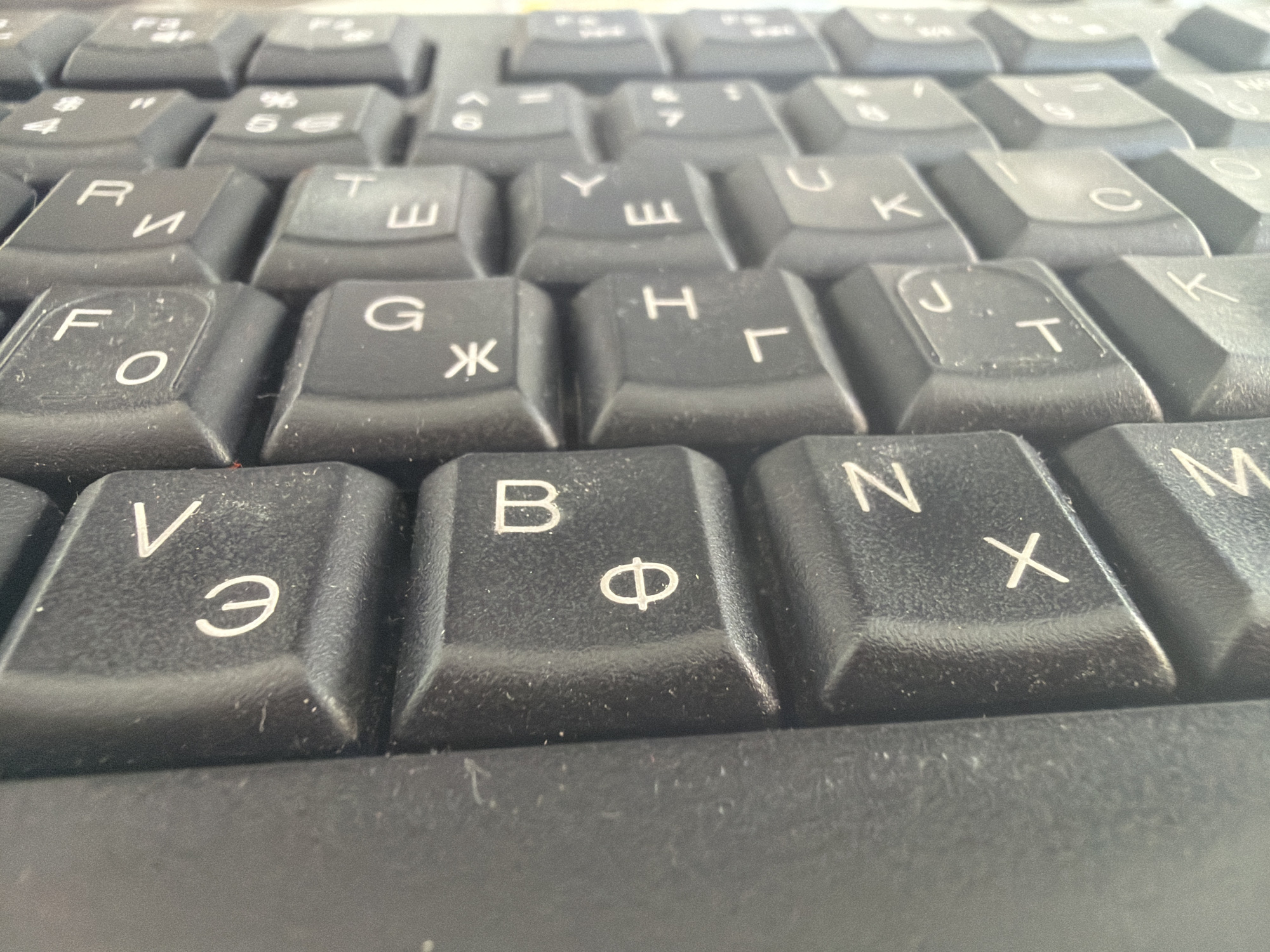 This image is a close-up of a computer keyboard. The keys are black with white letters and symbols. The layout appears to be a combination of Latin and Cyrillic characters, suggesting a keyboard for a language that uses both scripts, such as Bulgarian. The image shows a partial view of the keyboard, focusing on the middle section of the letter keys. The keyboard seems dusty.
Given the Cyrillic characters, the city of Plovdiv, Bulgaria could be a plausible location for where the image was taken.