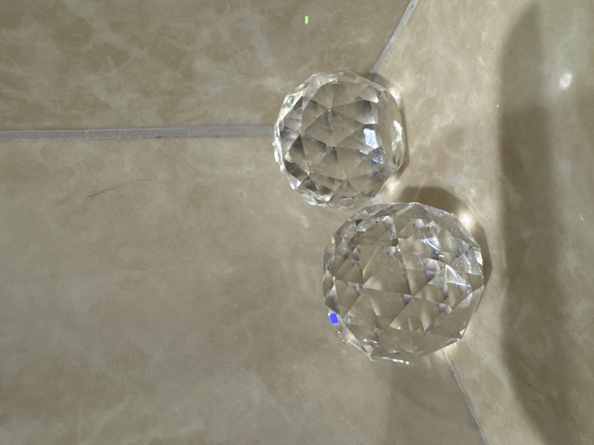 The image shows two faceted crystal balls resting on a beige tiled surface. The tiles appear to be part of a floor or wall. The location is unspecified.