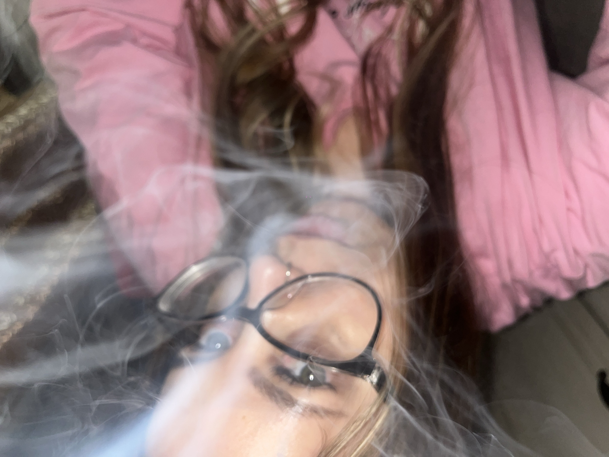 A close-up photograph, partially obscured by smoke, shows a person wearing glasses and a pink shirt. The setting and location within Novopokrovskaya, Russia are indiscernible due to the image's focus and the obscuring smoke.