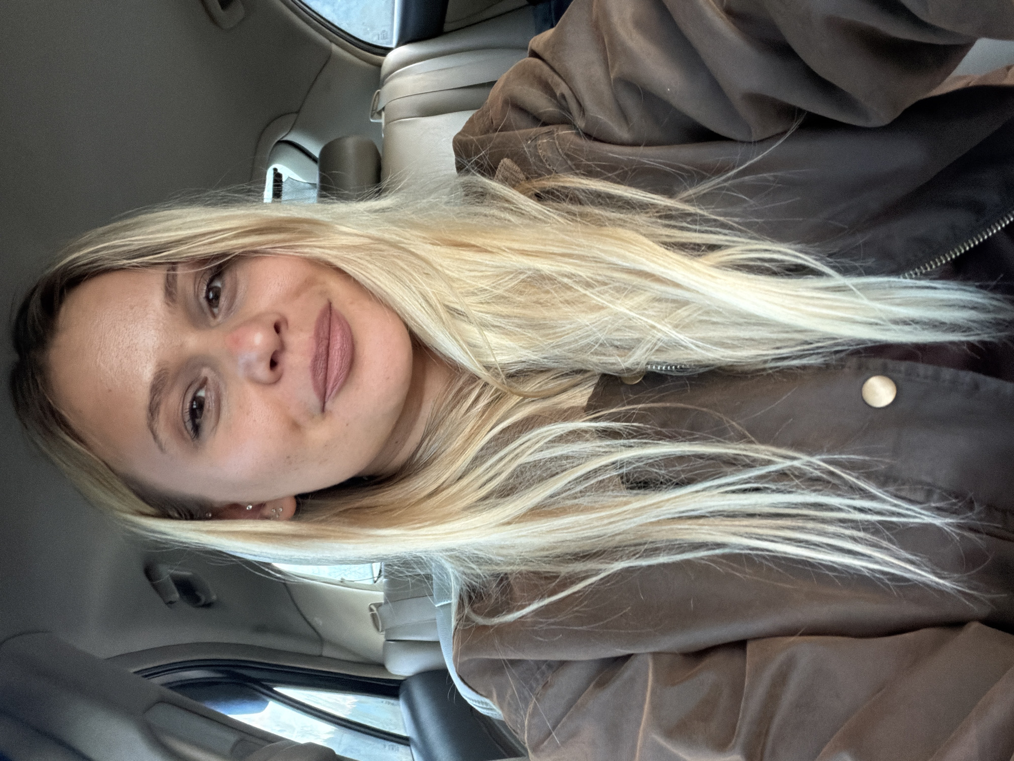 The image depicts a woman with long, blonde hair in the front passenger seat of a car. She is wearing a brown jacket. The interior of the car is visible, including the dashboard, seats, and window. The location in Дулесово, Russia, cannot be confirmed from the image.