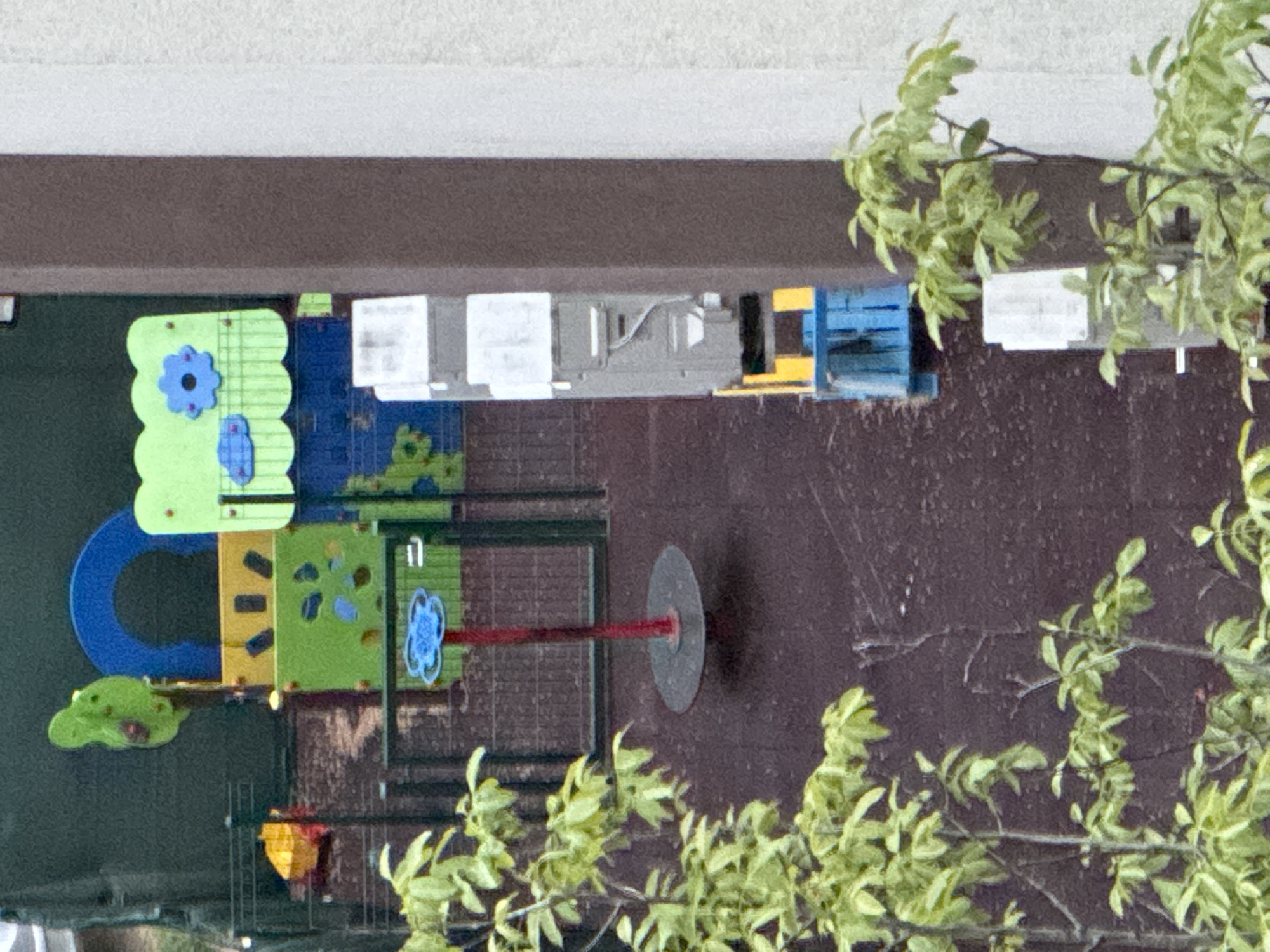 The image depicts a playground with a variety of colorful play structures, including climbing walls, slides, and other interactive elements. The playground is located in Sofia, Bulgaria. The presence of plants and trees suggests an outdoor setting. The image is oriented upside down.