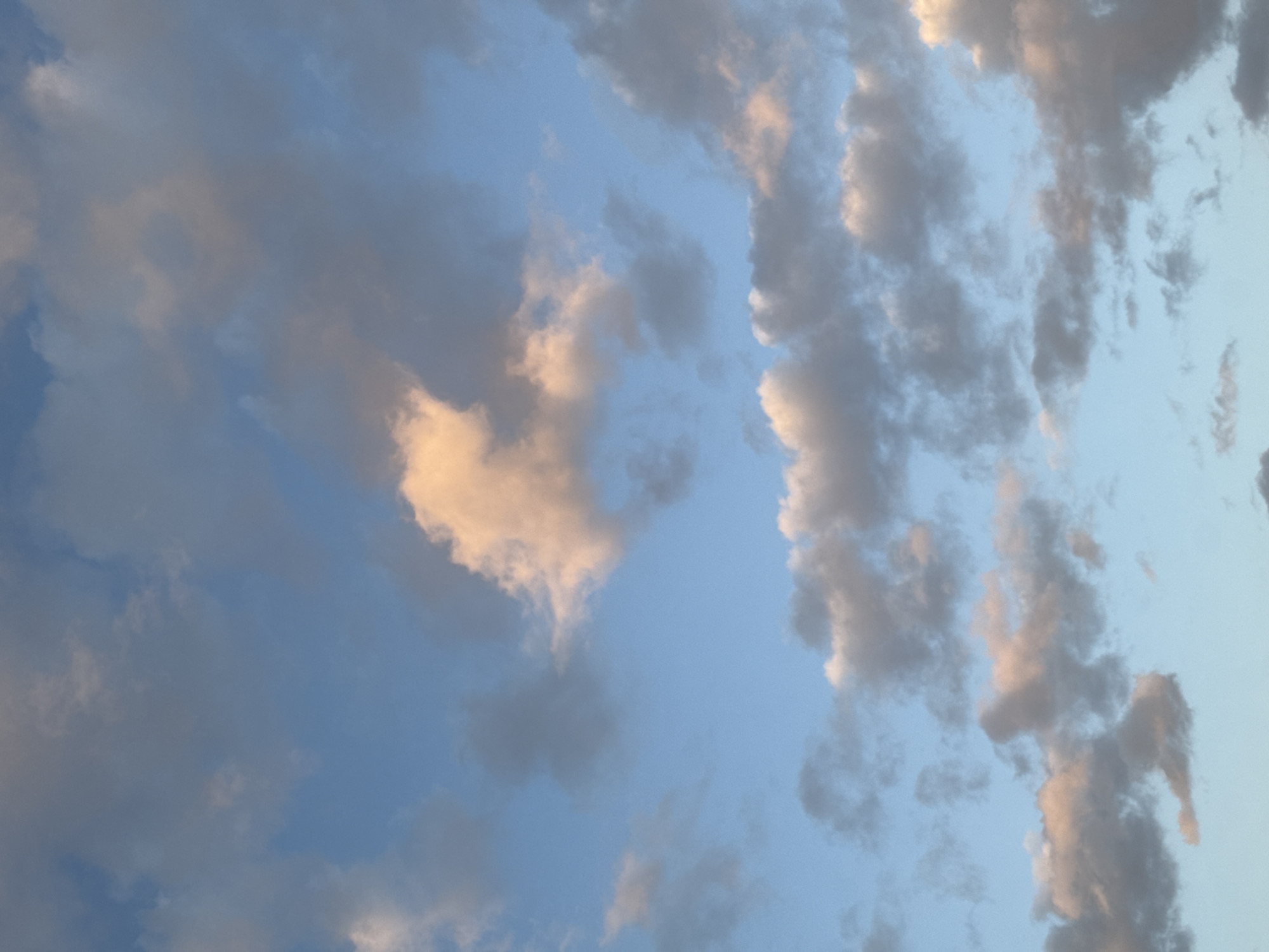 The image shows a sky with clouds. The sky is light blue. The clouds are various shades of grey and white. There is no indication of a specific location, or of Łódź, Poland, in the image. There are no people, subjects, objects, actions, or interactions visible.