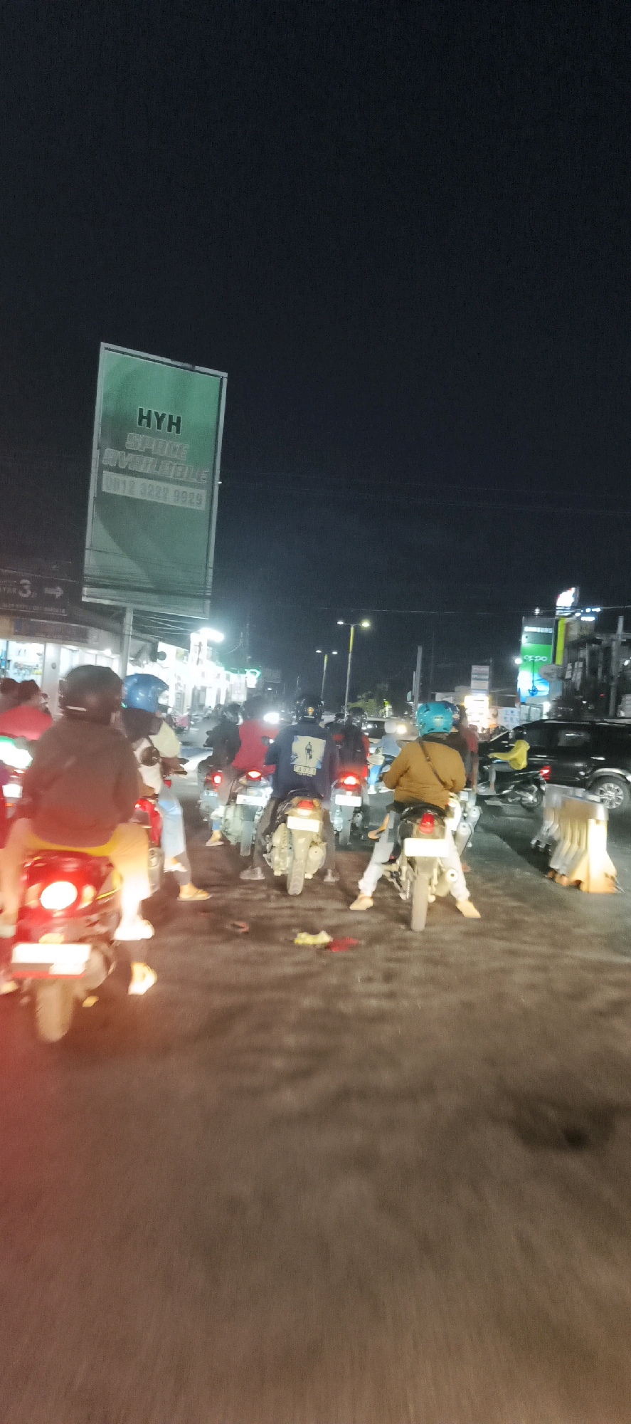 The image shows a busy street scene at night in Calukan RT 1 RW 5 Keboansikep, Indonesia. A group of people are riding motorbikes in traffic. The motorbikes are varied in color and style, with some riders wearing helmets. The street is lined with shops and businesses, some of which are lit with neon signs. The sky is dark, indicating that it is nighttime. There are streetlights and the headlights of the motorbikes illuminating the scene. The overall impression is one of a vibrant and active urban environment at night.