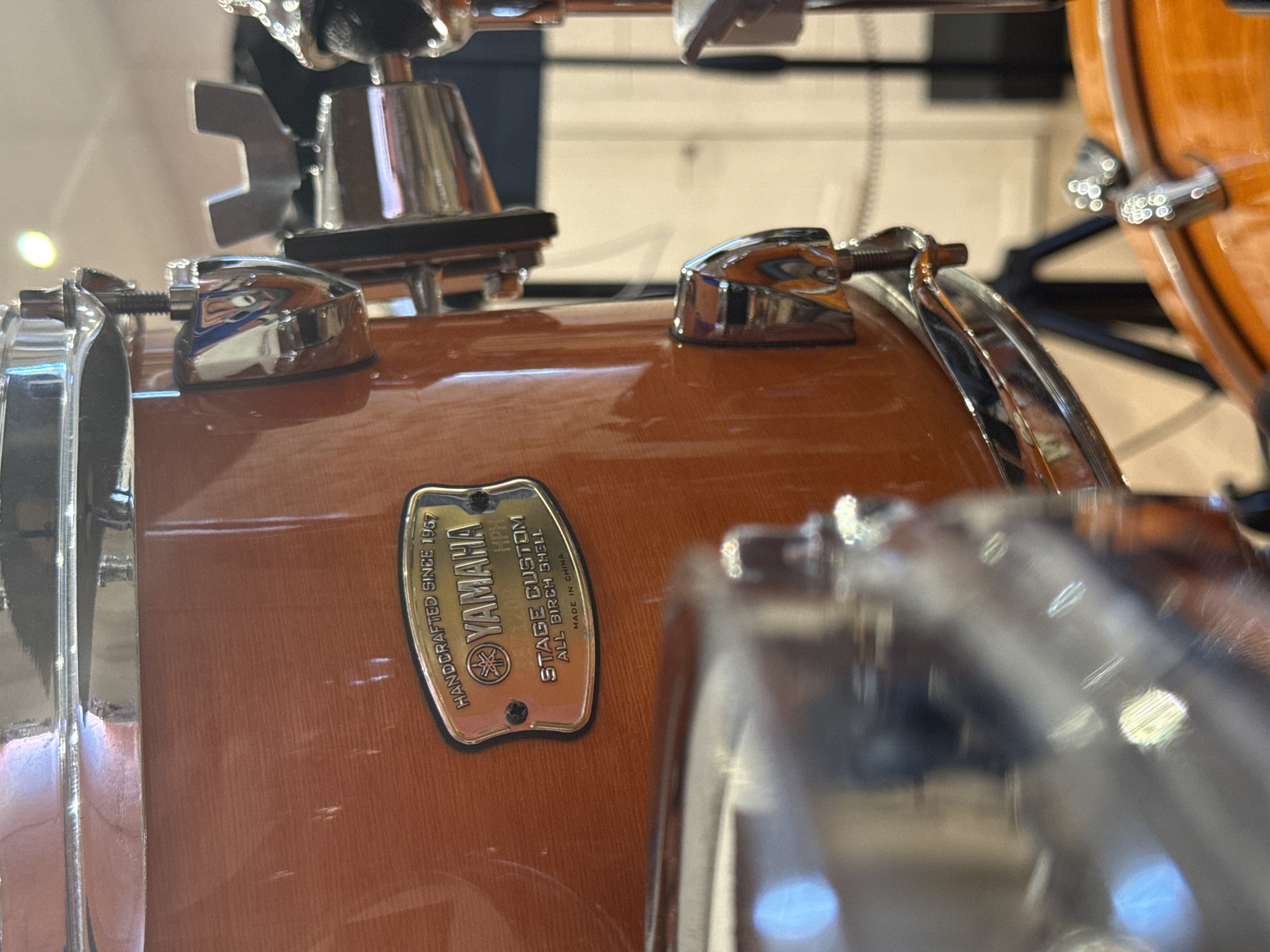 The image shows a close-up of a Yamaha Stage Custom drum. The drum has a natural wood finish. A badge on the drum reads "YAMAHA HANDCRAFTED SINCE 1967 STAGE CUSTOM ALL BIRCH SHELL MADE IN CHINA." There are chrome drum lugs and hoops visible. Another drum is partially visible in the background.
The image does not provide any information about the city of Shcherbinka, Russia.