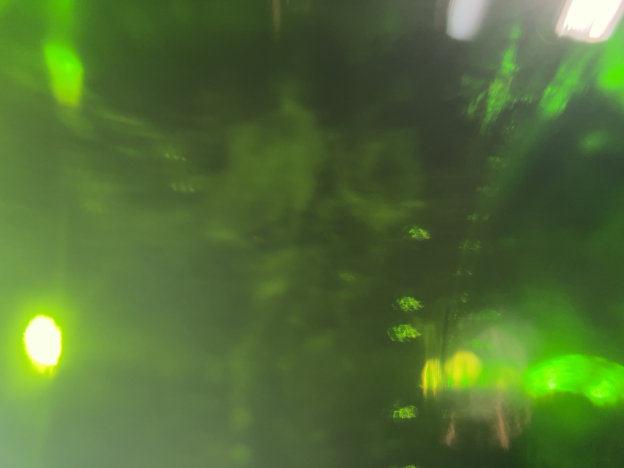 The image appears to be a blurry photograph taken in a dark, possibly indoor environment. The dominant color is green, with various points and areas of bright light creating significant visual distortion. The nature of the light sources is ambiguous, but they may be street lights seen through fog or a window.
Based on the assumption that it might be the City of Newburgh, United States of America, the location is inferred. Without more information, it's difficult to specify the exact place within Newburgh or the time the photo was taken.