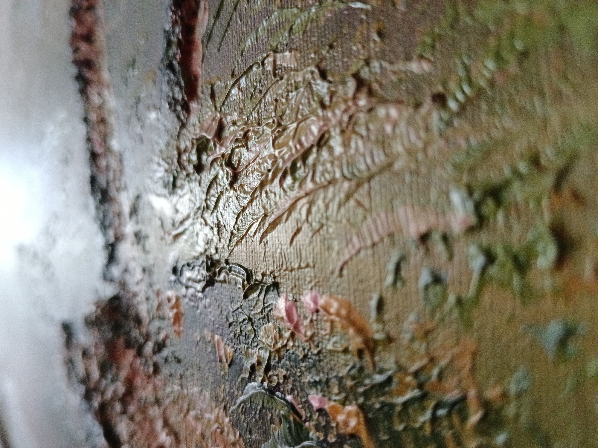 The image is a close-up, abstract shot of a textured painting. The paint is applied thickly, creating a three-dimensional quality with visible brushstrokes and ridges. The dominant colors are earthy tones of brown, green, and hints of pink and white. The lighting highlights the texture of the paint, creating shadows and giving the surface a glossy sheen in some areas. There are no discernible objects, people, or actions; the focus is entirely on the material and textural qualities of the artwork. The image does not provide any information or visual cues that could be used to determine its location in Severnyi, Russia, or any other specific geographic context.