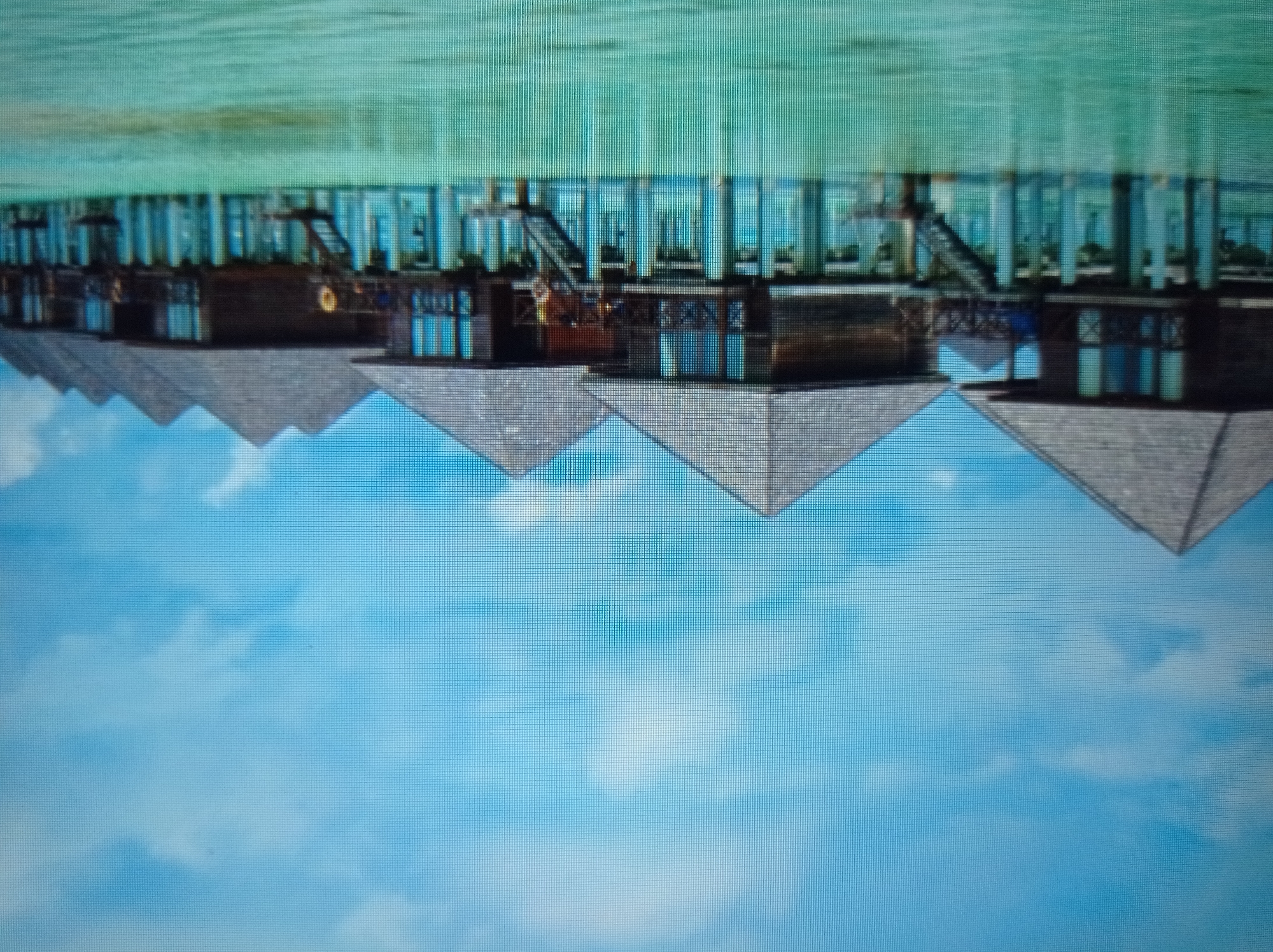 The image depicts a row of overwater bungalows in a tropical setting. The bungalows are constructed of dark wood with pyramid-shaped roofs. They are supported by stilts above a body of clear, turquoise water. A bright blue sky with scattered white clouds forms the backdrop. The scene suggests a resort or a vacation destination, likely in a warm climate. There are no people visible in the image. The location is not the city of Mukachevo, Ukraine, as the environment does not match the climate or architecture of that region.