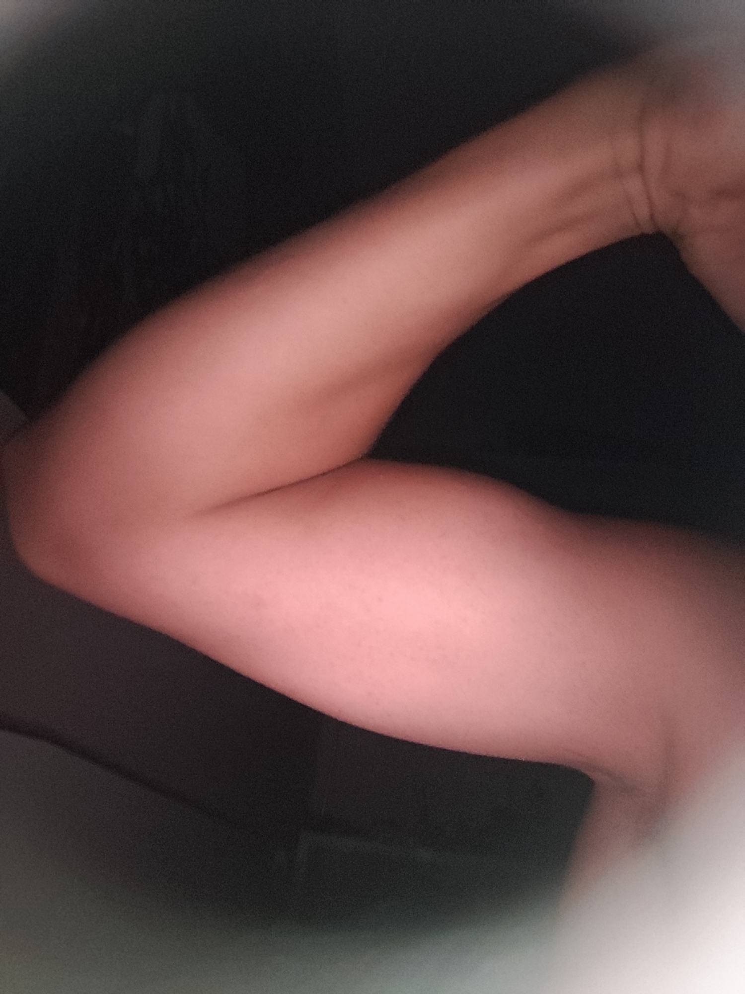 An arm is shown from the elbow to the shoulder, bent at the elbow. The skin is pinkish and there are some very fine hairs visible. The background is dark and blurry, with some indistinct shapes suggesting a dimly lit indoor environment. The image is not clear enough to determine the specific location in Pomorie, Bulgaria.