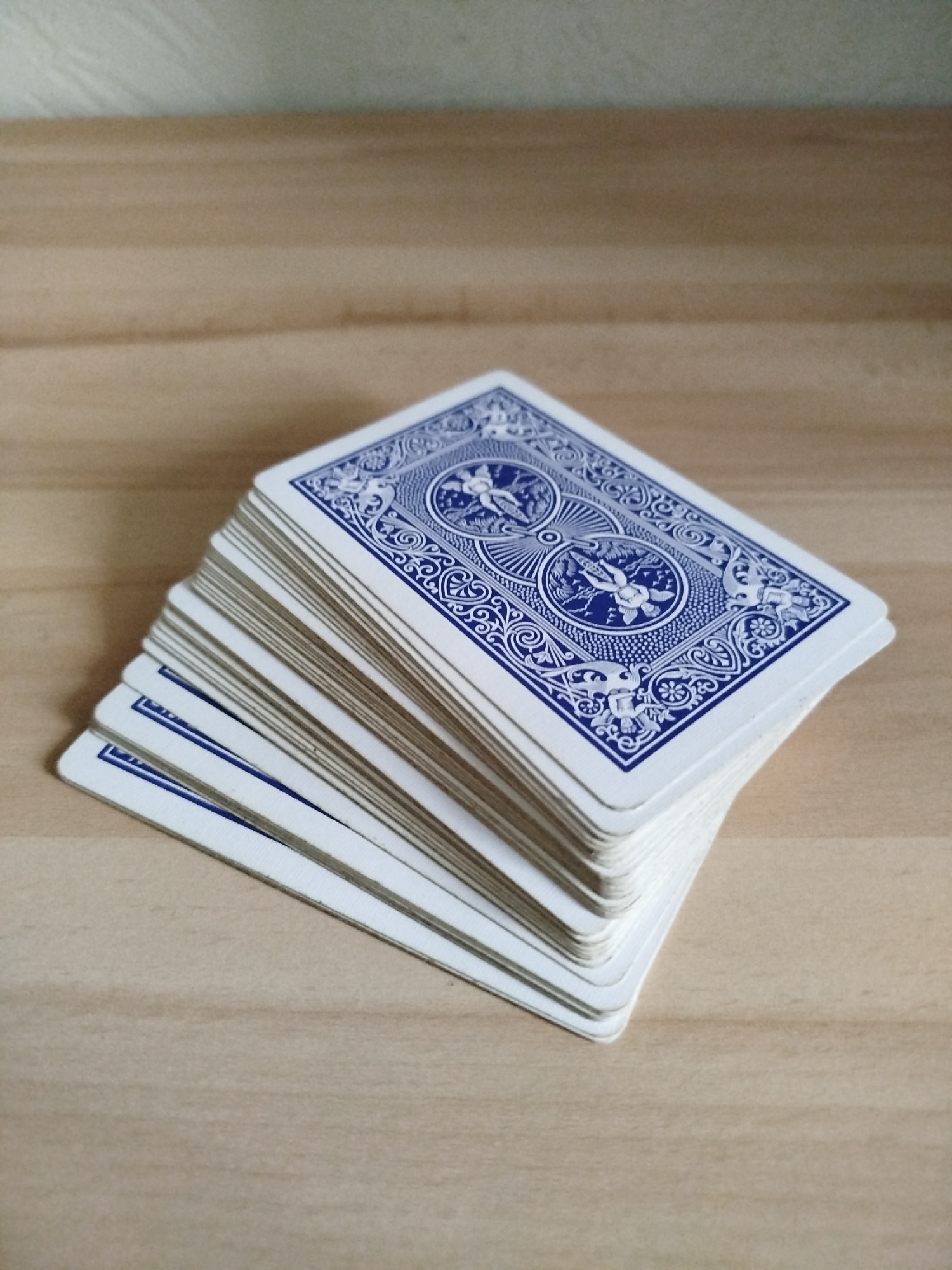 A deck of playing cards with blue patterned backs is stacked on a light brown wooden surface. The scene does not provide any information to indicate the location in the city of Varna, Bulgaria.