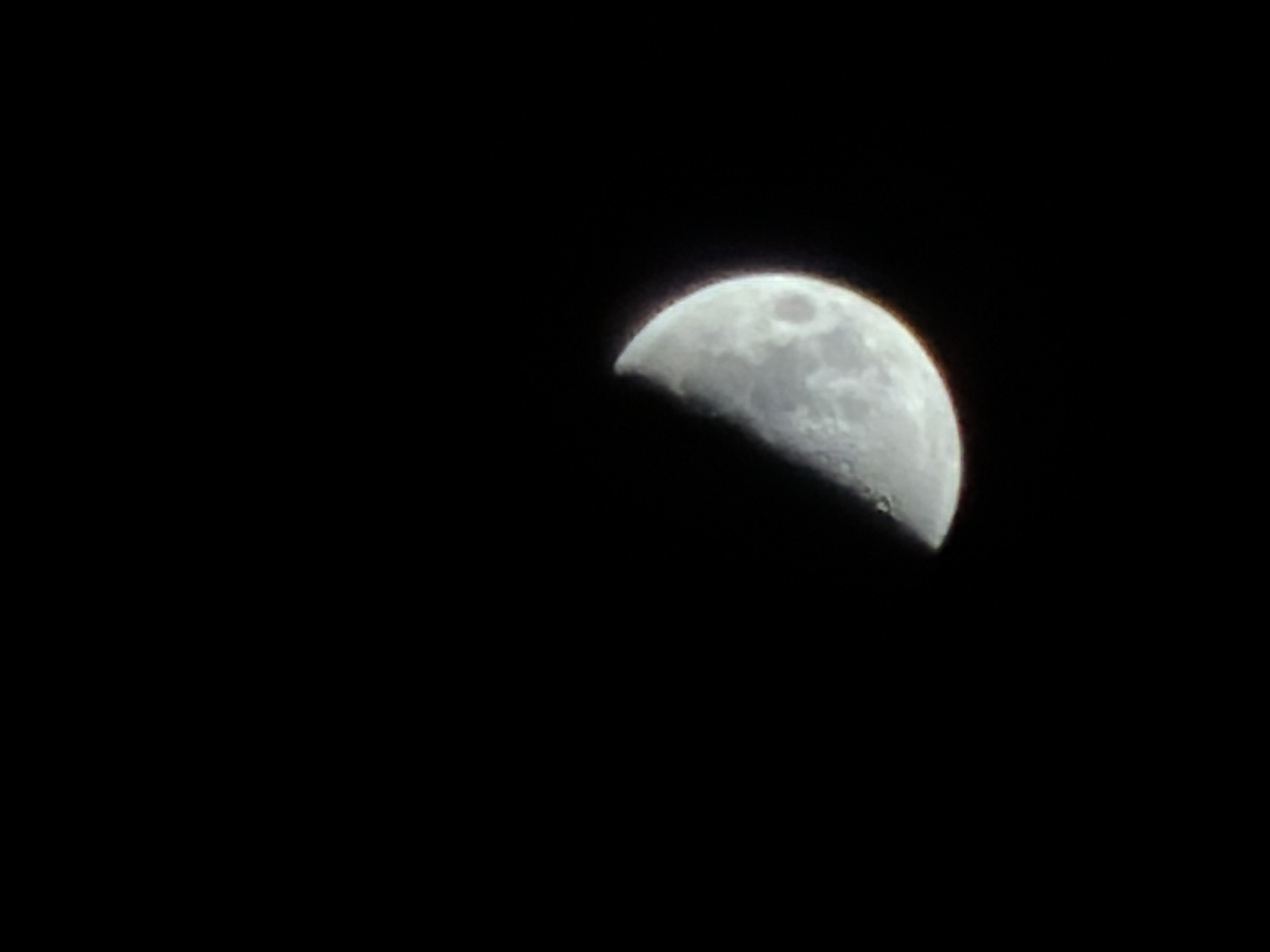 The image presents a detailed close-up of the Moon against a completely black night sky, observed from Izhevsk, Russia. The Moon is captured during its waxing gibbous or first quarter phase, with approximately half of its visible surface brightly illuminated. Distinct lunar features, including various craters and darker mare regions, are clearly discernible across the illuminated portion, showcasing the rugged texture of the lunar landscape. The terminator, the line separating the illuminated and dark parts of the Moon, is sharp, highlighting the relief of its features.
The black background signifies a clear, starless night, free from clouds or atmospheric haze, which allowed for an unobstructed view of the celestial body. No other objects, individuals, or signs of human activity are present in the frame. The photograph's focus is exclusively on the Moon, suggesting an astronomical observation. There is no visible text or specific event taking place beyond the natural state of the Moon in the night sky. The image conveys a sense of calm and the vastness of space through its singular, well-defined subject.