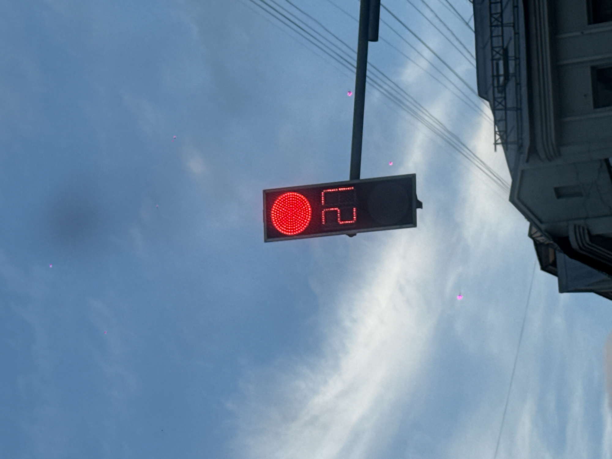 The image shows a traffic light in Moscow, Russia. The light is red, and a digital display next to it shows the number "22," presumably counting down the time remaining before the light turns green. The traffic light is attached to a pole and wires are visible above it. A building is visible on the right side of the image and the sky is a cloudy blue.