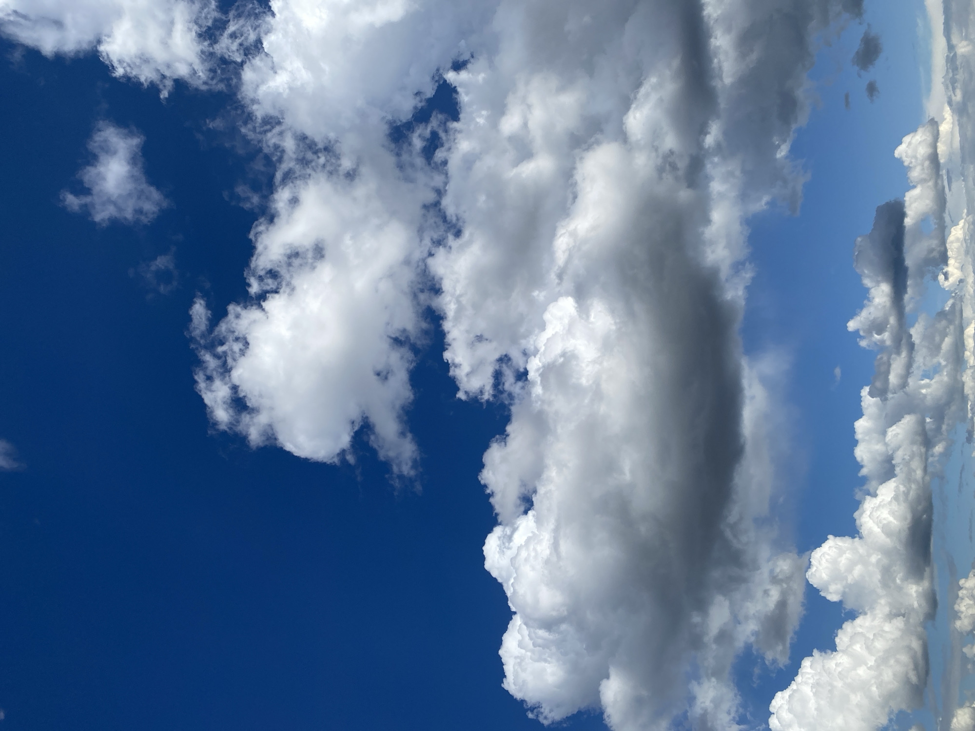 The image captures a daytime sky filled with clouds. The left side of the frame features a deep blue, cloudless sky. Moving towards the right, the sky is increasingly covered with puffy, white cumulonimbus clouds. Some of the clouds appear shaded in gray, indicating varying levels of sunlight and thickness. The clouds are scattered throughout the frame. The location is Unknown, Unknown.