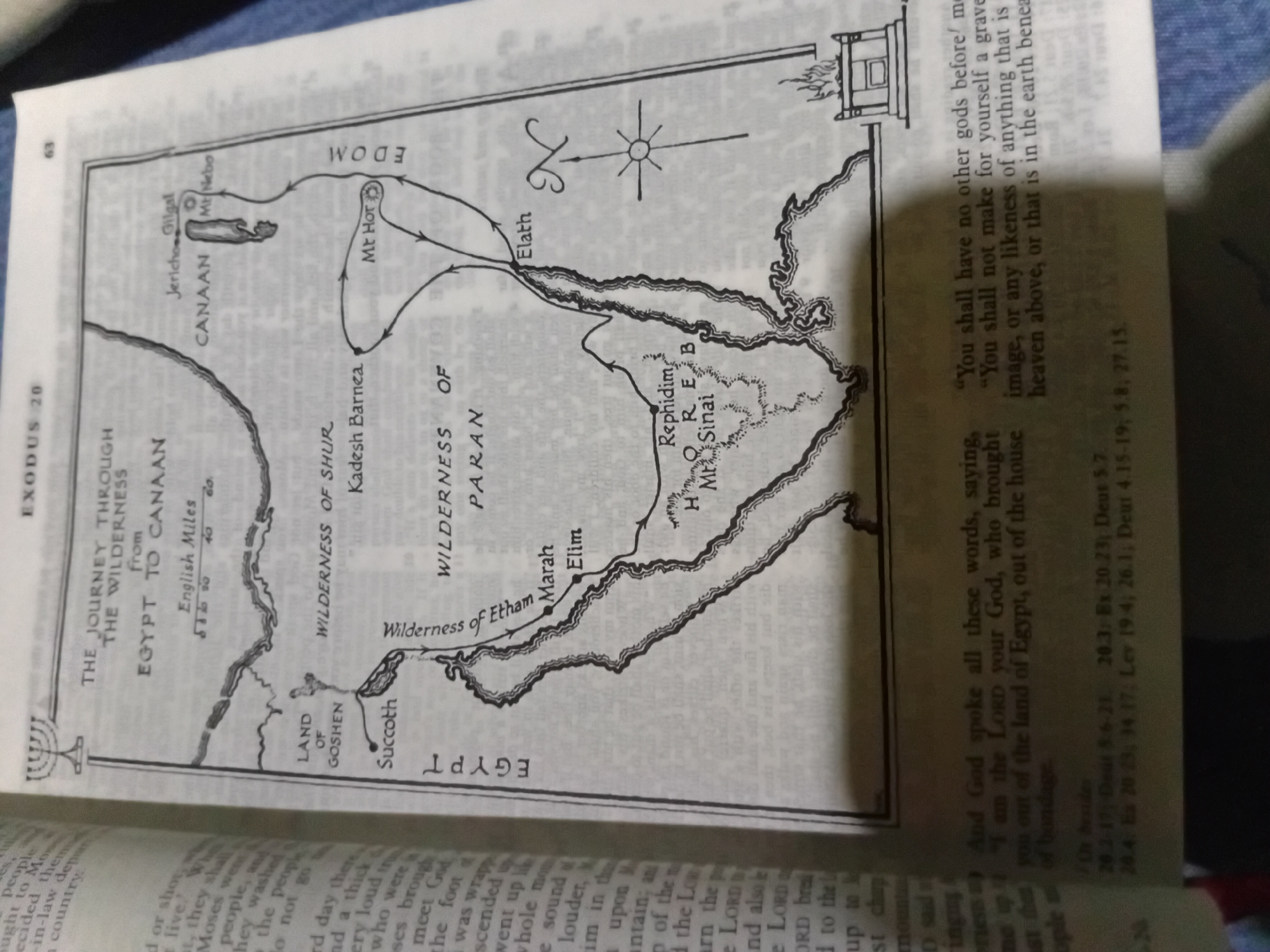 The image displays a page from a book, specifically showing a map and text. The map illustrates "The Journey Through the Wilderness" from Egypt to Canaan, detailing various locations and routes taken. It includes place names like the Land of Goshen, Succoth, Wilderness of Shur, Kadesh Barnea, Mt. Hor, Edom, Elath, Marah, Elim, Rephidim, and Mt. Sinai. The text below the map appears to be biblical verses from Exodus and Deuteronomy, referencing the Ten Commandments. The background is a textured surface, possibly a table or cloth, in muted tones. There are no people or actions depicted in the image; it is a static visual presentation of educational or religious content. The city of Nkpor, Nigeria is not depicted or referenced in this image.