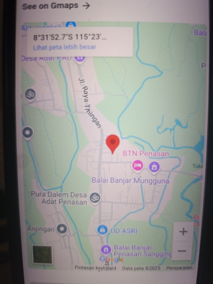 The image shows a screen capture of Google Maps. The coordinates of the location shown in the map are 8°31'52.7"S 115°23'... The location is Kecamatan Arjasa, Indonesia. The map shows the following features: a road labeled "Jl. Raya Thingan," a place called "BTN Penasan," "Balai Banjar Mungguna," "Pura Dalam Desa Adat Penasan," "Anjingan," "UD ASRI," "Balai Banjar Penasan Sangging," and "Desa Adat Penasan." There is a red marker on the map indicating the location. The screen also shows a blue button that says "See on Gmaps" and a button that says "Lihat peta lebih besar". The bottom of the screen shows text in Indonesian that says "Pintasan keyboard" (keyboard shortcut), "Data peta ©2025" (Map data ©2025), and "Persyaratan" (Requirements). There is a green icon, a blue circle, and a pink icon at various locations on the map. The map is set in a dark gray and white color scheme.