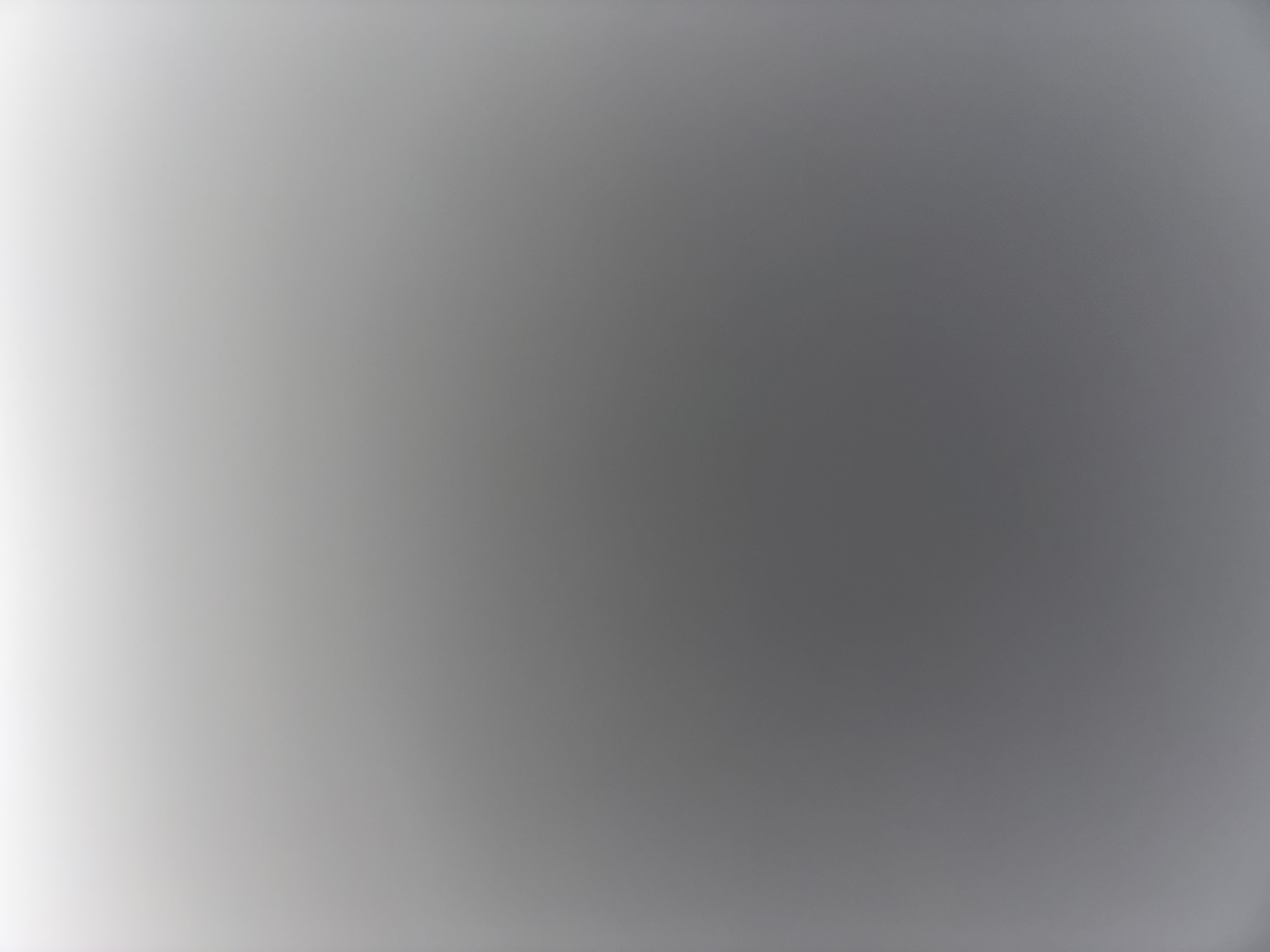 The image is a blurry, out-of-focus gradient ranging from near-white in the lower left corner to a medium gray in the upper right corner. No specific location, subjects, or objects are discernible. No actions or interactions are visible.