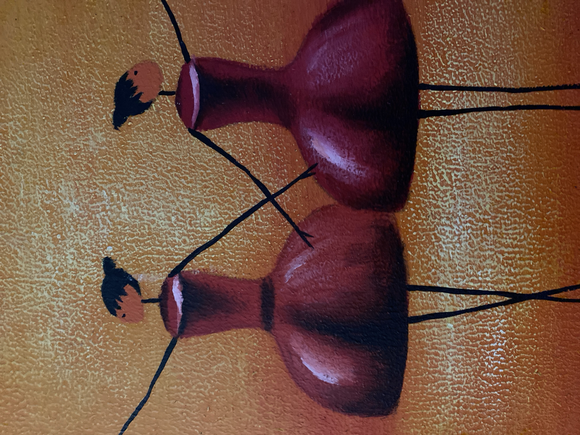 The image is a close-up of a painting featuring two abstract figures. The figures are depicted with reddish-brown bulbous bodies, small orange heads with black "hair," and thin black lines representing limbs. The figures are positioned one above the other, with the lower figure appearing as a reflection of the upper one. The background is a textured mix of orange and yellow. The style is simplistic and artistic. There is no evidence to identify this image as being in or near Budva, Montenegro.