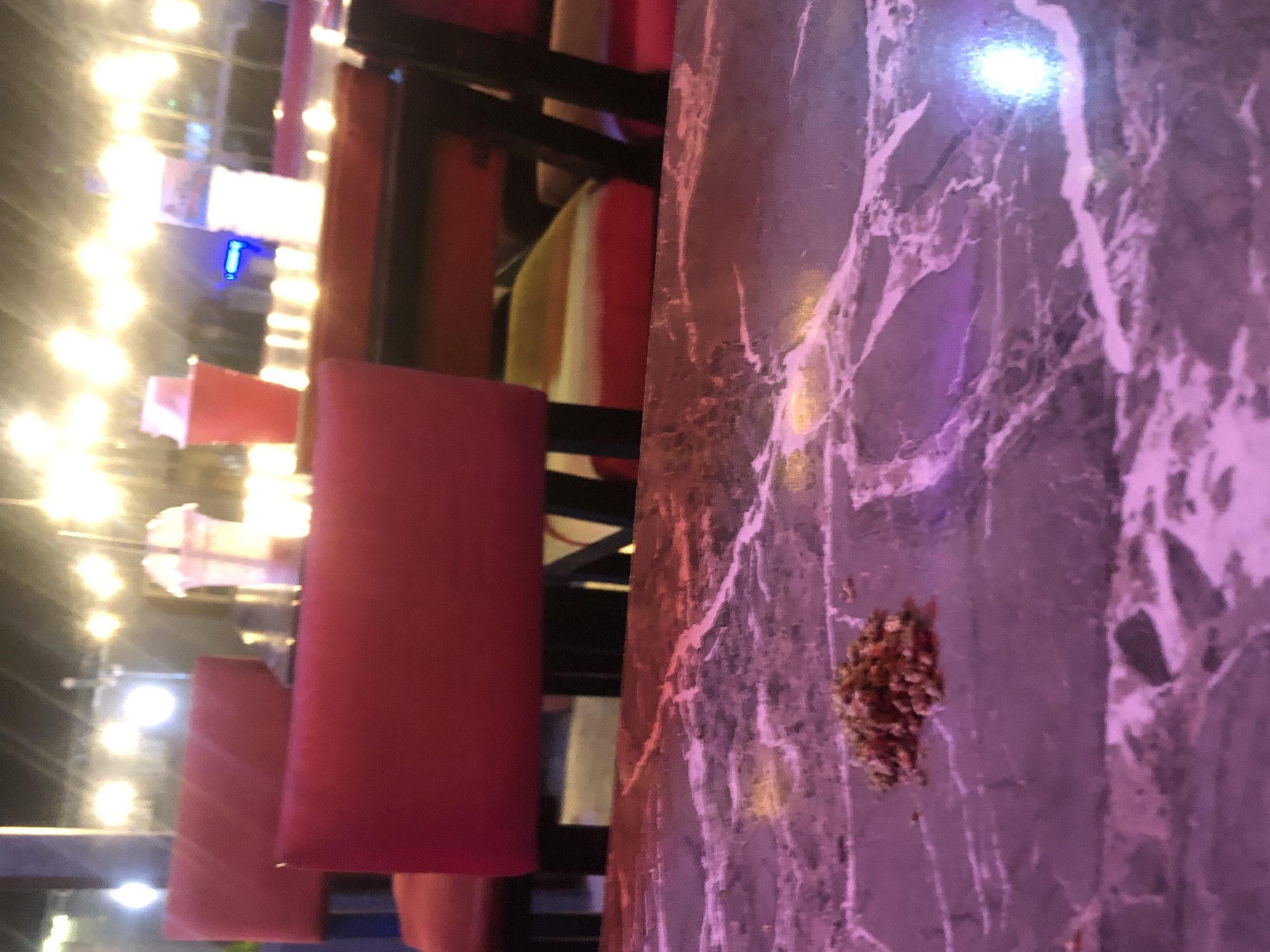 A pile of crushed herbs is on a marble table at night. In the background, red chairs are visible, along with blurred lights and drinks on tables. The image is likely taken at an outdoor seating area of a restaurant or bar on Rukuba Road, Nigeria.