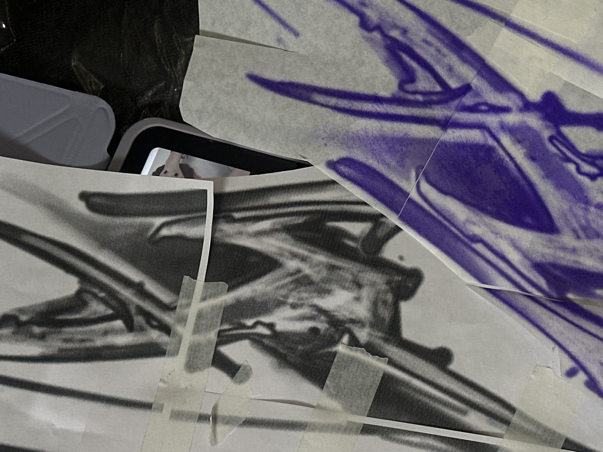 The image shows a close-up of a collection of papers with abstract designs in black and purple ink, taped together. The papers are layered on top of each other, partially obscuring a smartphone lying underneath. The edge of a white container is also visible on the left. The image does not reveal any information to indicate it was taken in Moscow, Russia.