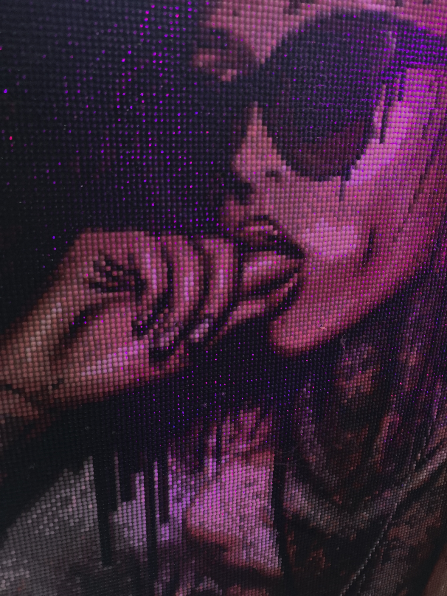 The image is a close-up of what appears to be a diamond painting depicting a person wearing sunglasses with their fingers near their mouth. The color scheme is predominantly shades of pink and black with some purple highlights. The individual's face is partially obscured by the sunglasses. The background is dark. The diamond painting gives the image a textured, pixelated appearance.
It does not take place in Noviy, Russia and this is likely a detail hallucinated by the model.
