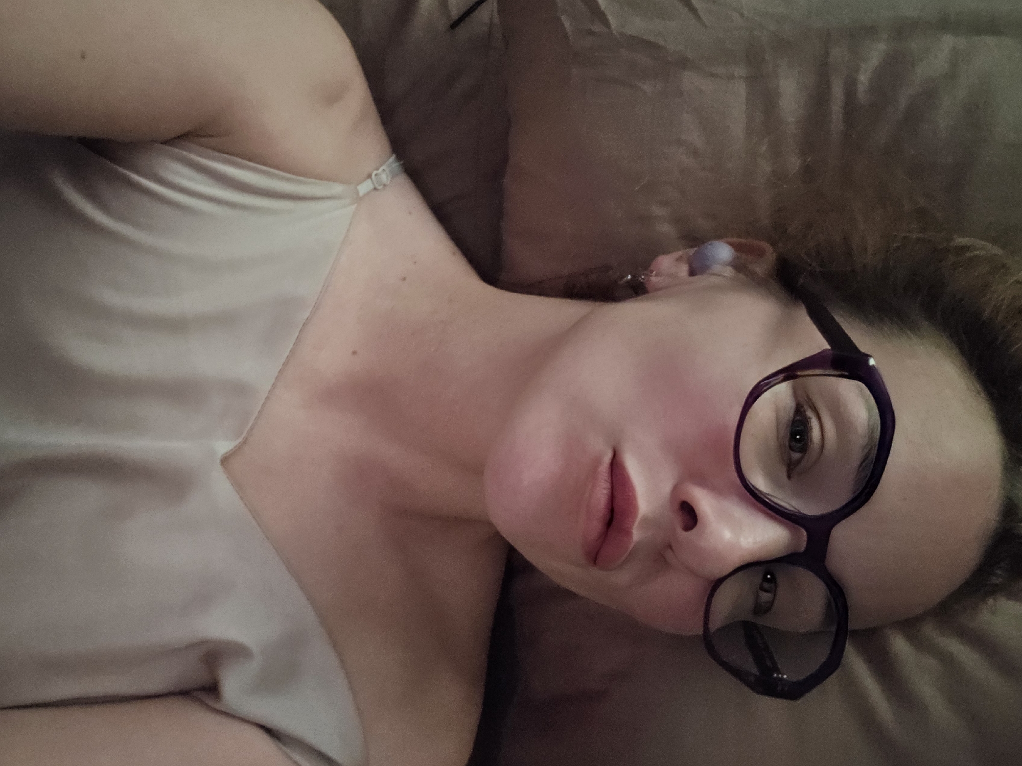 A woman is lying on a brown pillow, wearing glasses and a light-colored tank top. The location is not discernable as Sochi, Russia.