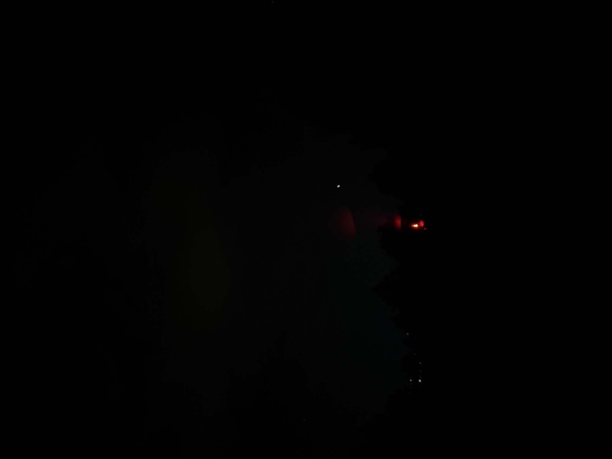 A dark, underexposed image shows a cluster of lights in the night. The lights appear red and white, partially obscured by the darkness, suggesting a potential light source within a dimly lit environment. The image lacks clear definition of other surroundings, making it difficult to ascertain specific details about the location or objects present. There is no additional information about location or people.