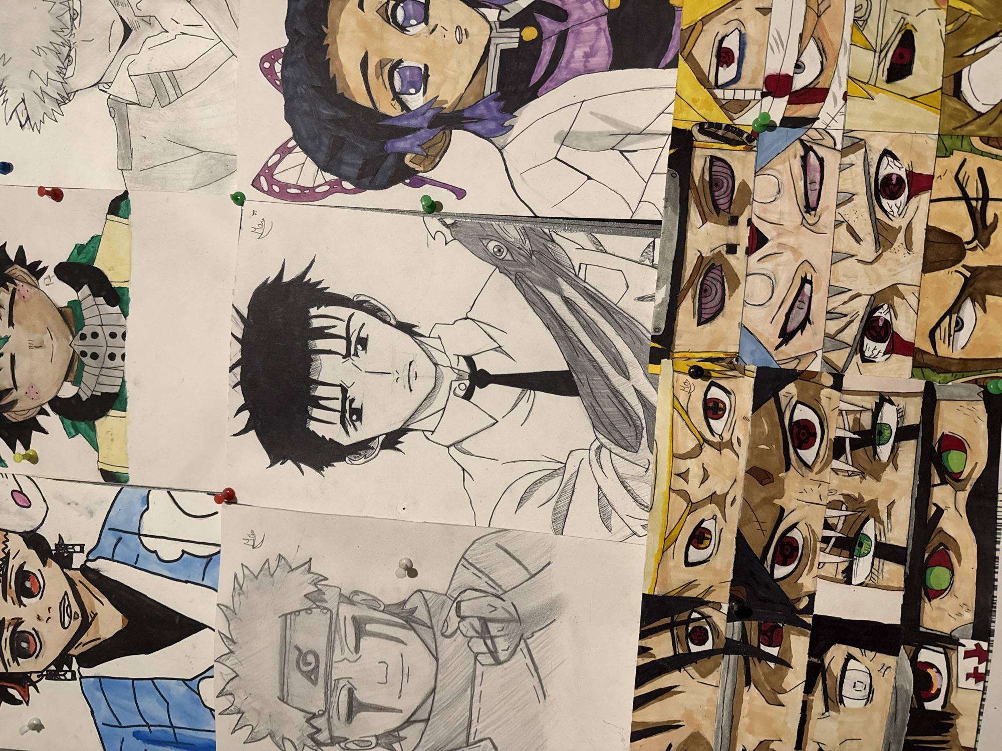 A collection of numerous anime and manga fan art drawings is displayed, pinned onto an unseen vertical surface, likely a wall or bulletin board. The drawings are arranged closely together, with some overlapping.
The artwork features a variety of characters, rendered in both color and black-and-white pencil sketches. On the top left, a partial pencil sketch of Katsuki Bakugo from My Hero Academia is visible. Below it, there's a colorful drawing of a character, possibly from Demon Slayer, in green and yellow attire.
The upper-middle section features a vibrant, colored portrait of Shinobu Kocho from Demon Slayer, characterized by her purple eyes and butterfly-themed hair ornament. Below her, a black-and-white pencil sketch portrays Giyu Tomioka, also from Demon Slayer, in a suit, holding a sword.
On the bottom left, a colorful drawing of Tanjiro Kamado from Demon Slayer is depicted wearing a blue and white maid-like outfit. To its right is a pencil sketch of Naruto Uzumaki from Naruto, wearing his headband and holding a clenched fist.
The entire right side of the image is dominated by a collage of vertical strips of paper, each featuring multiple anime-style eyes. These eyes exhibit various colors, including red, purple, and green, and some display distinct patterns such as the Sharingan and Rinnegan from Naruto.
The drawings are secured by pushpins of various colors: red, green, white, blue, and black. A faint signature, "Hos" or "Hgs," is visible on several drawings, including near Shinobu's head and on some of the eye strips. The scene captures a vibrant display of fan art, showcasing diverse characters and artistic styles.