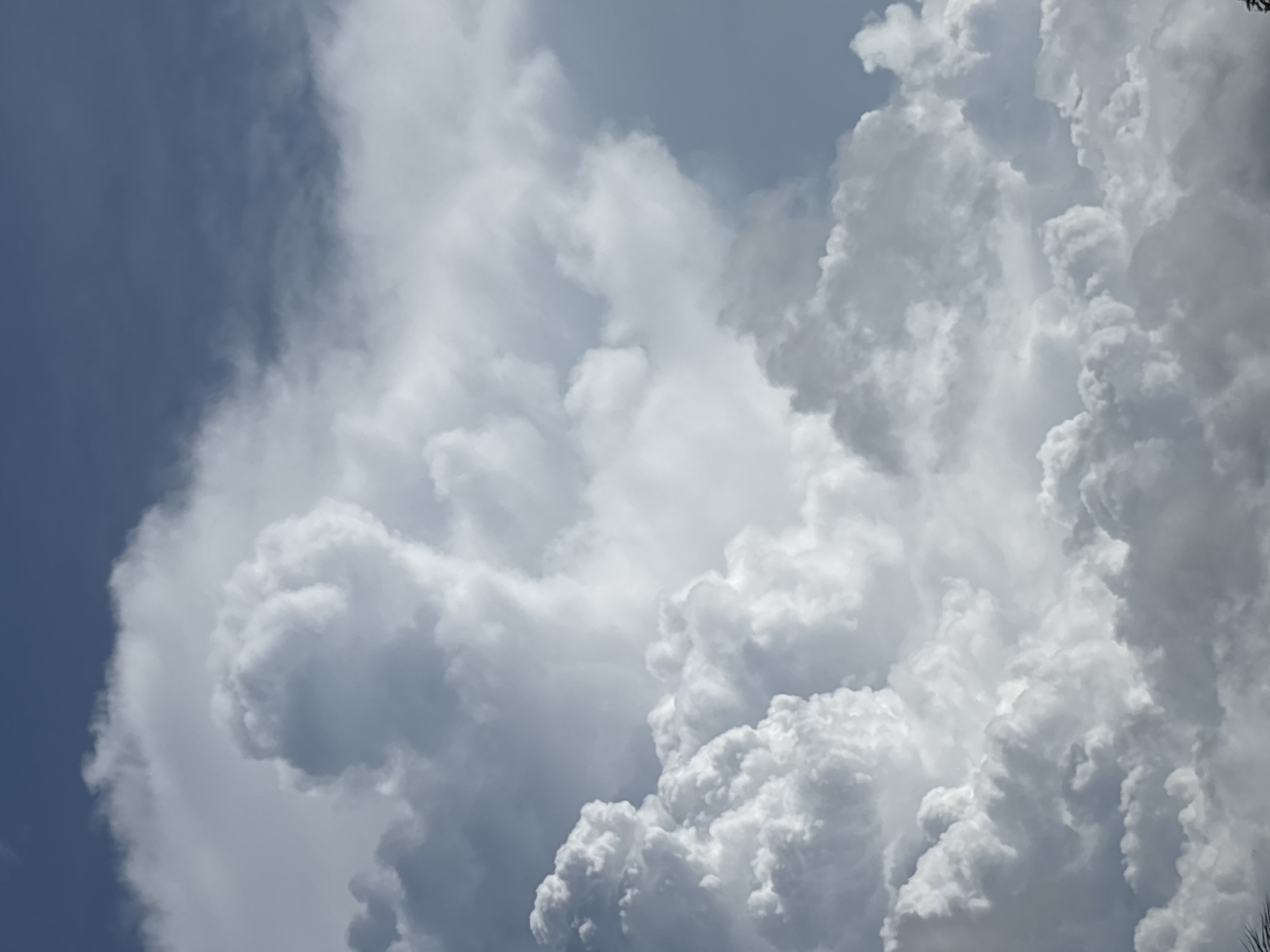 The image shows a view of the sky filled with cumulus clouds. The left portion of the frame reveals a patch of blue sky, while the majority is dominated by large, puffy white clouds of varying sizes and densities. The clouds appear to be towering, with intricate patterns and textures. The location is indicated as บ้านบางรักษ์, Thailand, though there are no discernable landmarks visible in the image to confirm the location. The photo captures a scene of dynamic cloud formation.