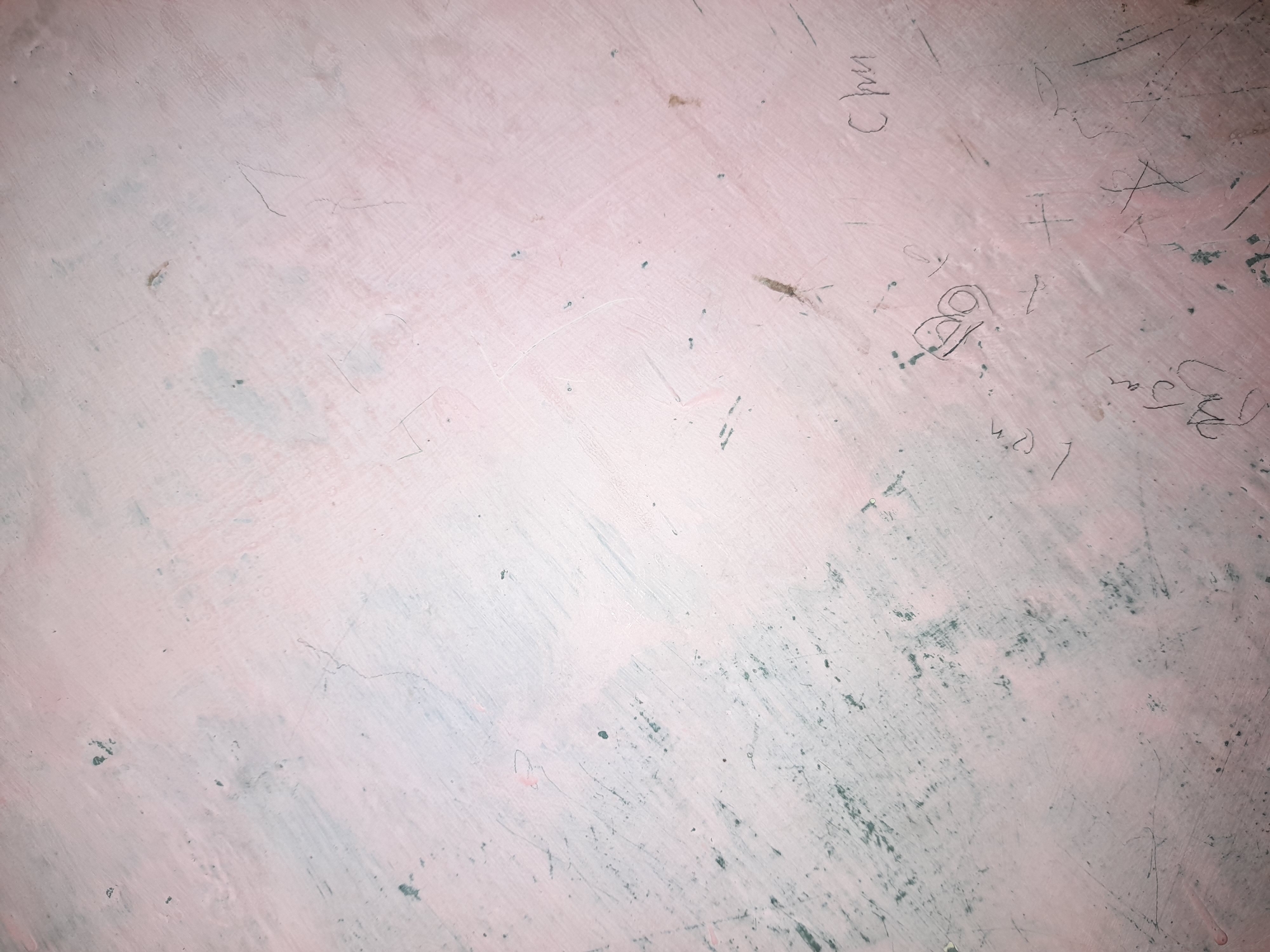 The image shows a close-up of a textured, pinkish surface with visible scratches and smudges. There are several instances of faint handwriting and markings on the surface, resembling graffiti or scribbles. Some of these markings are more prominent than others, appearing as dark lines and shapes. The texture of the surface suggests it could be a wall, a table, or some other painted or finished material. There are also some small, dark spots scattered across the surface, possibly dirt or paint chips. The lighting appears to be somewhat dim, casting subtle shadows and highlighting the textures. The overall impression is of an aged and possibly neglected surface that has been marked over time. There is no clear indication of a specific time of day, weather conditions, or a particular scene. The visible text appears to be in an Asian script, possibly Indonesian, with some Latin characters also present. The word "Chun" is clearly legible.