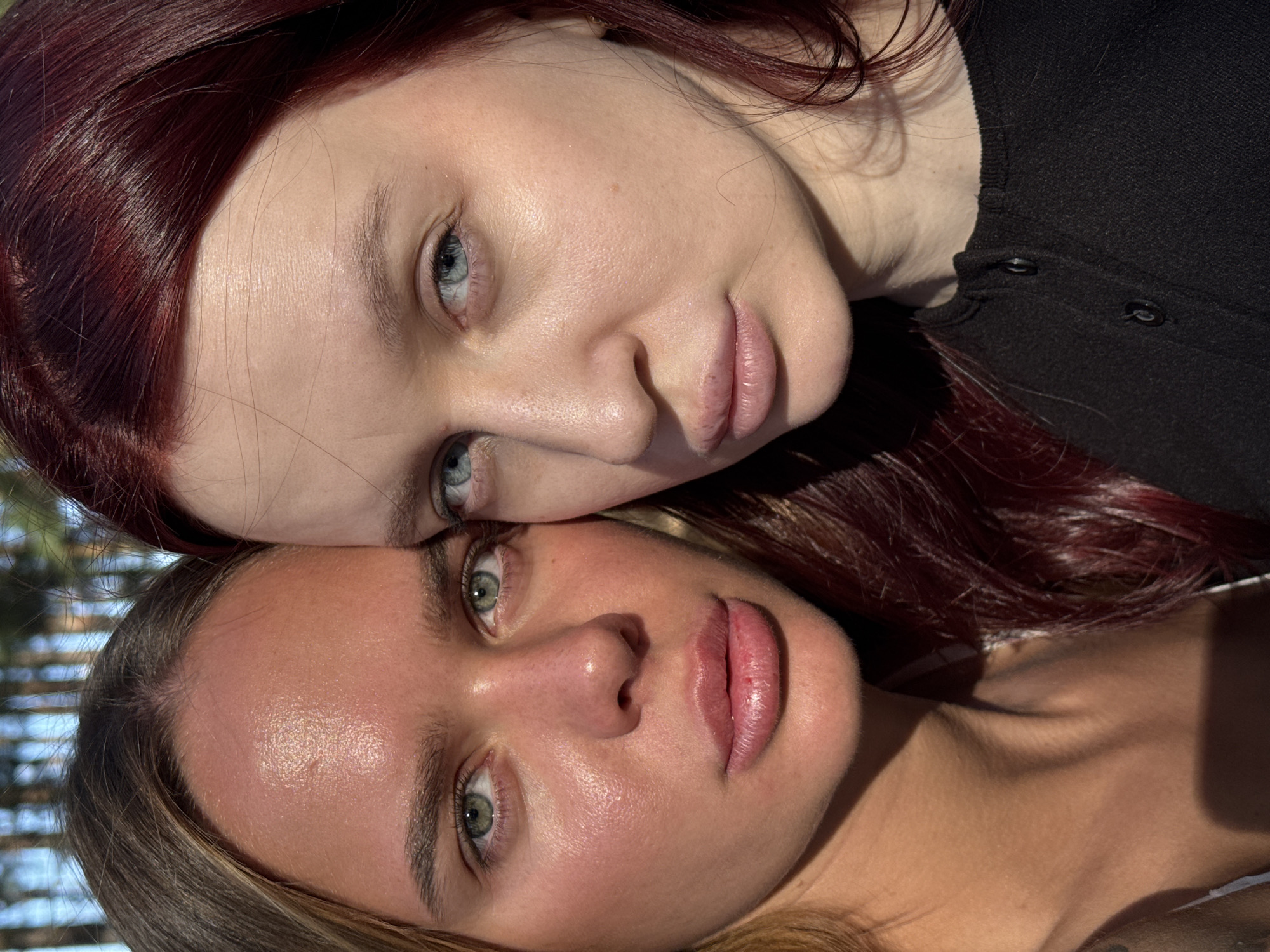 Two Caucasian women are posing for a close-up portrait. The woman on top has red hair and blue eyes and is wearing a black shirt. The woman on the bottom has brown hair and green eyes. Their faces are touching. The location is difficult to ascertain based on visual information alone, but it is not possible to confirm or deny the location is in Nizhny Novgorod, Russia based on the given image.