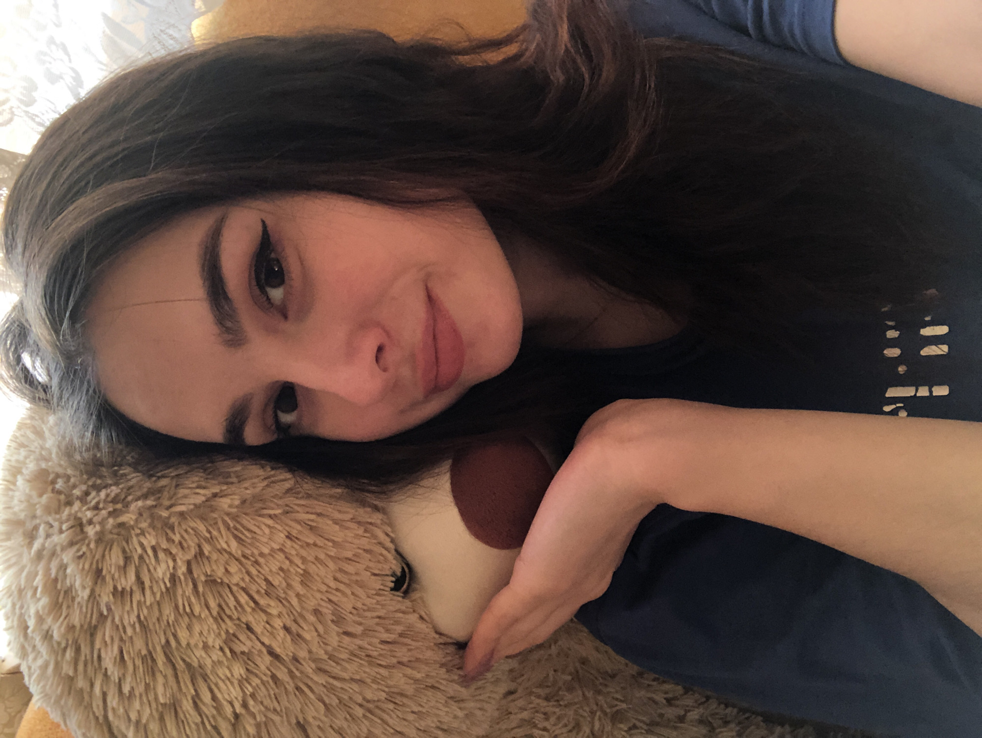 A young woman is lying on a large teddy bear. She is wearing a blue shirt. The location is not discernible from the image.