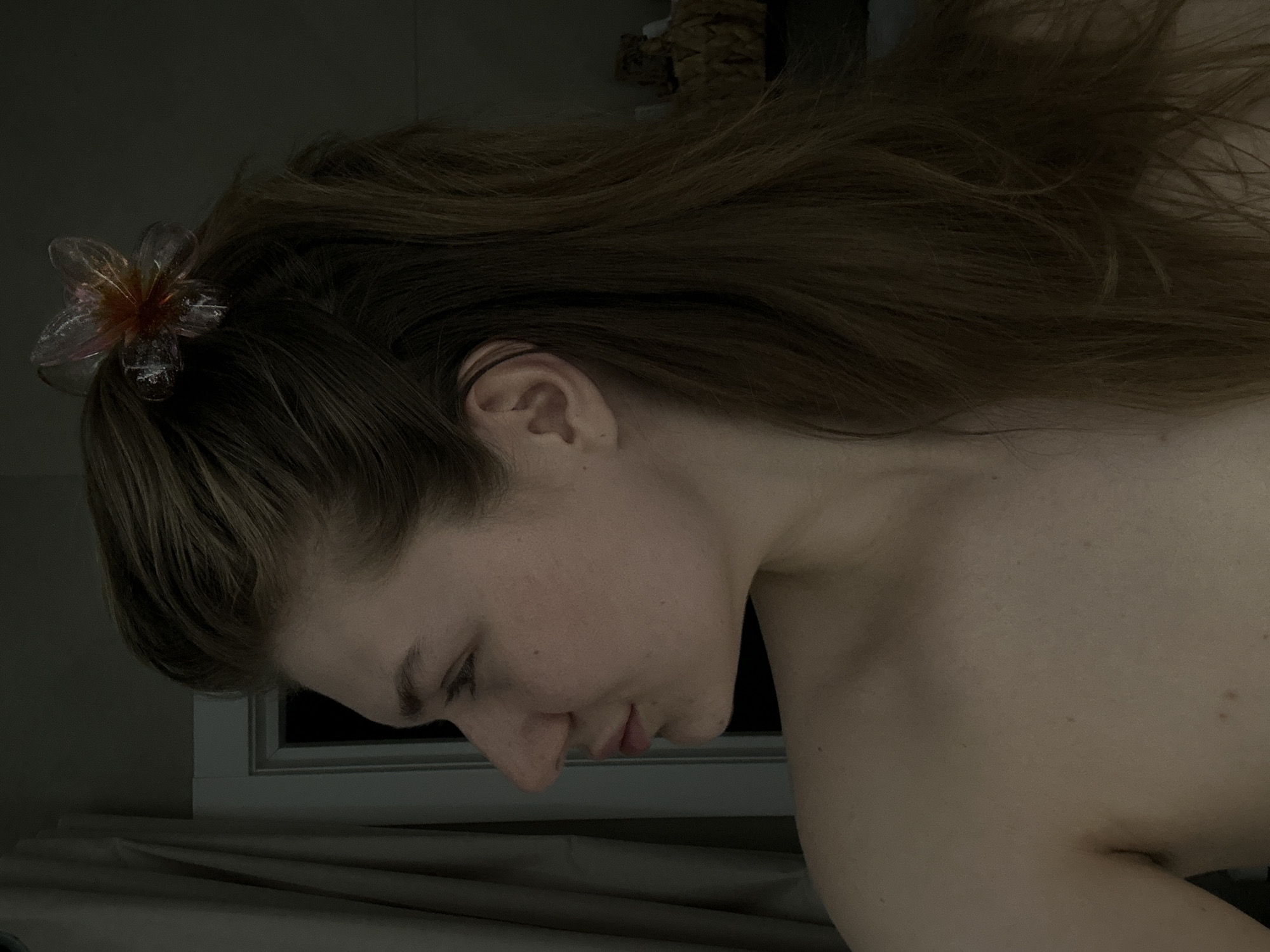 A close-up image shows a person with long brown hair, wearing a translucent flower clip in their hair. The person is positioned near a window. Due to lack of visual evidence, location cannot be verified.