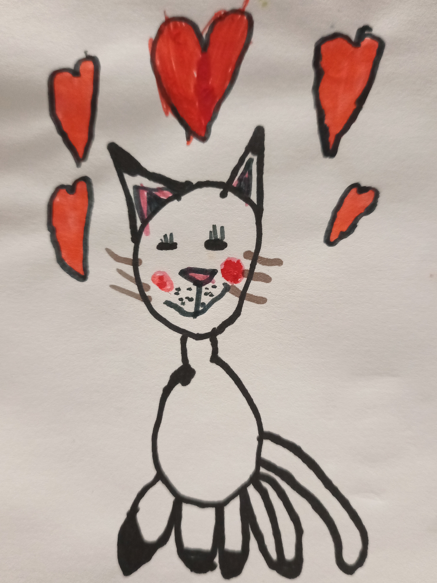 A child's drawing of a cat with red hearts floating around it is shown on a white background. The cat is white with black outlines and has pink blush marks on its cheeks. It has green eyes, a pink nose, and brown whiskers. The cat is sitting with its front paws on the ground and its tail extended behind it. There are five red hearts surrounding the cat. The drawing appears to be done with crayons or markers.